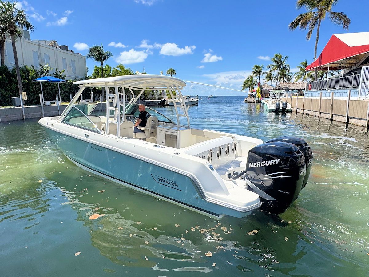 Blue and white motorboat with dual black engines in a waterway, person at the helm.