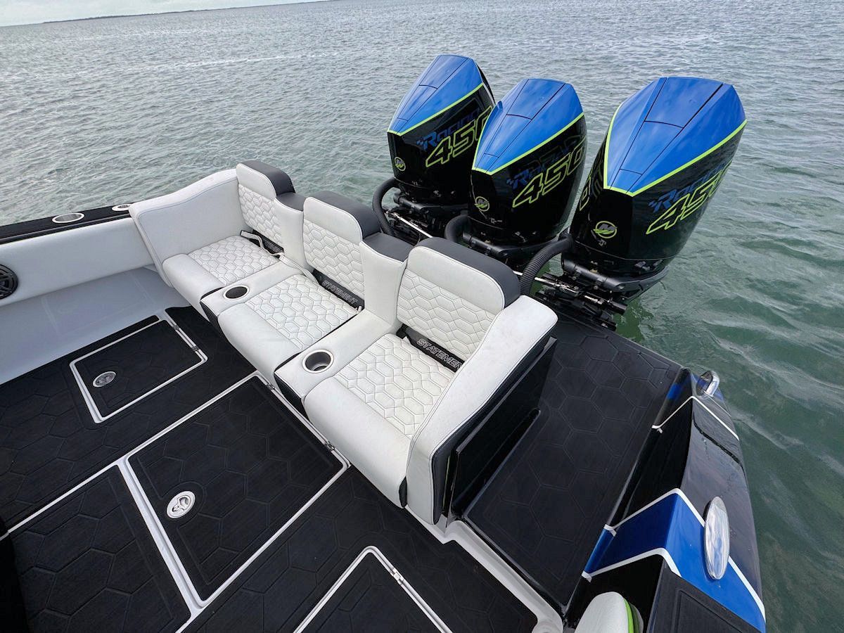 A high-speed boat with three blue outboard motors and white seating on the water.