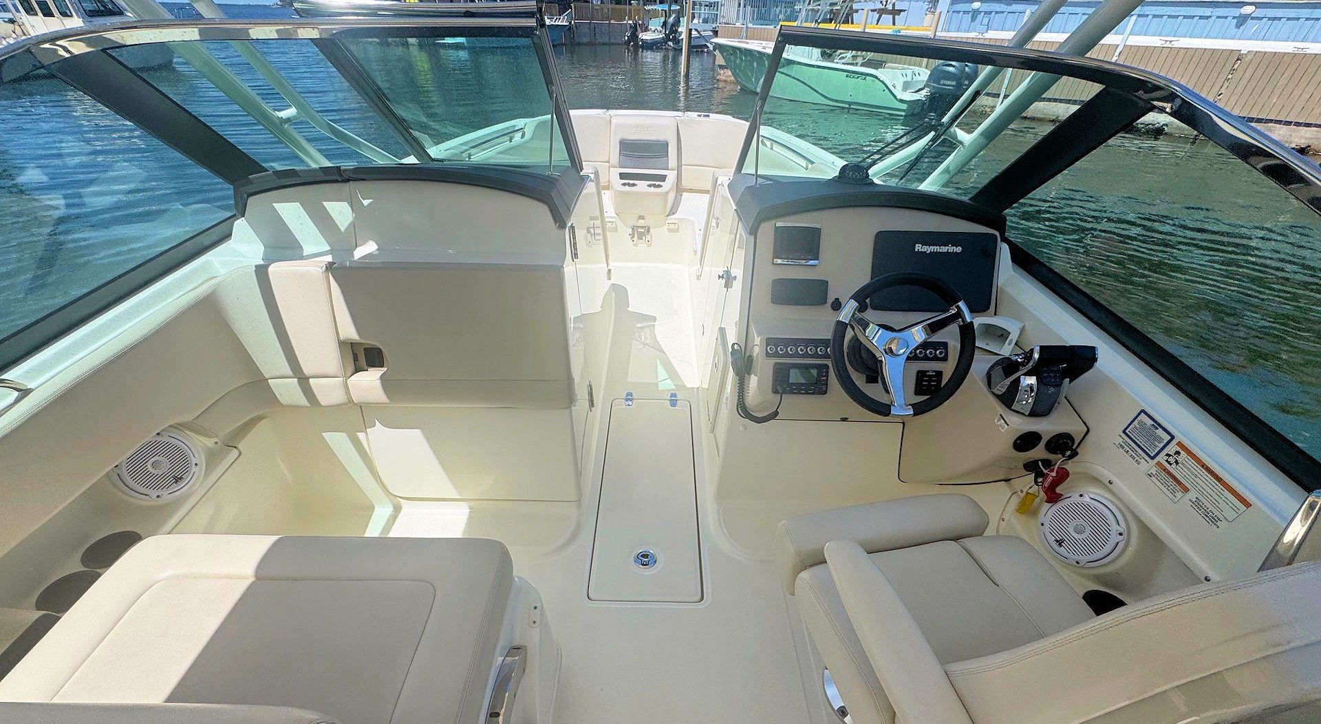 View from the helm of a cream-colored motorboat showing cockpit seating, a steering wheel, and a center walk-through.