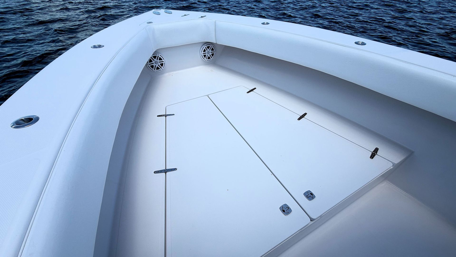 White boat deck with closed hatches and railings on calm blue water