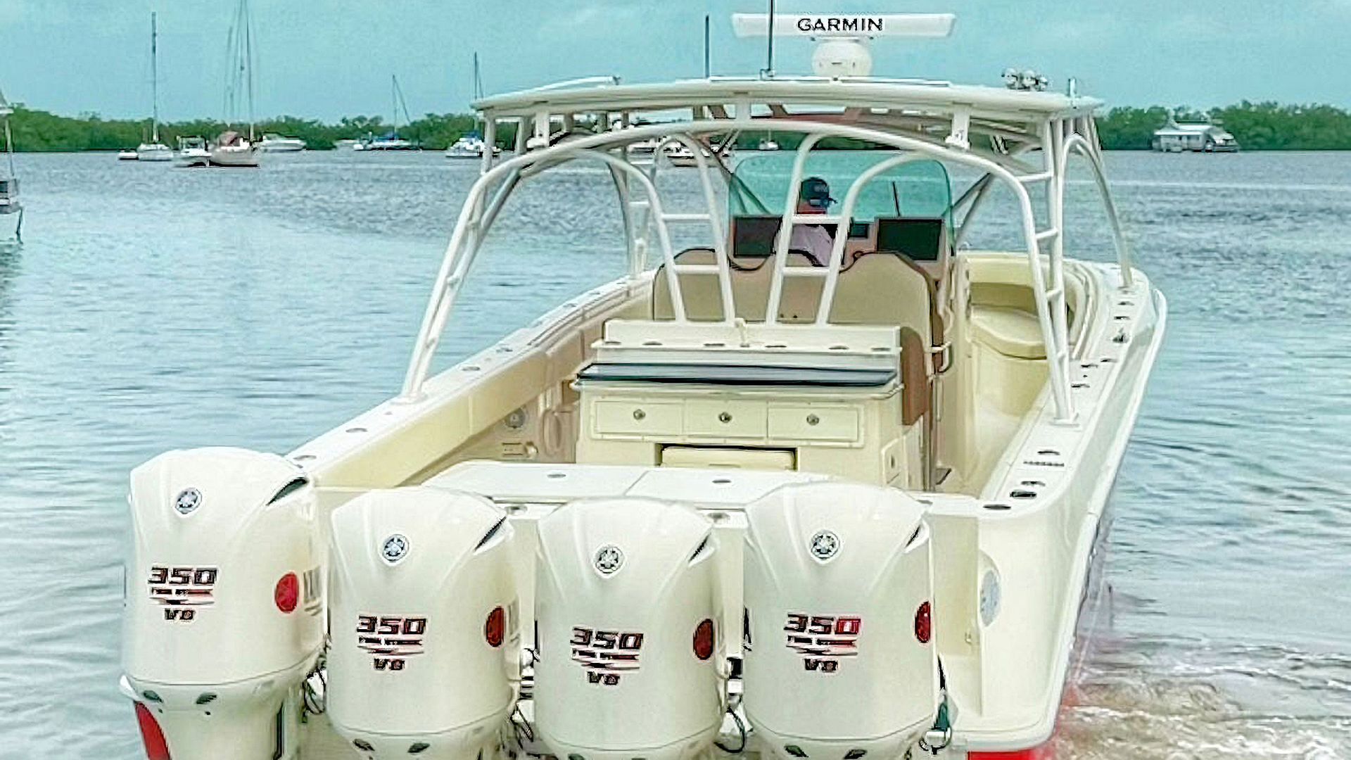 Red and white center console boat at a sandy shoreline, seen from the stern with four outboard engines and calm water beyond.