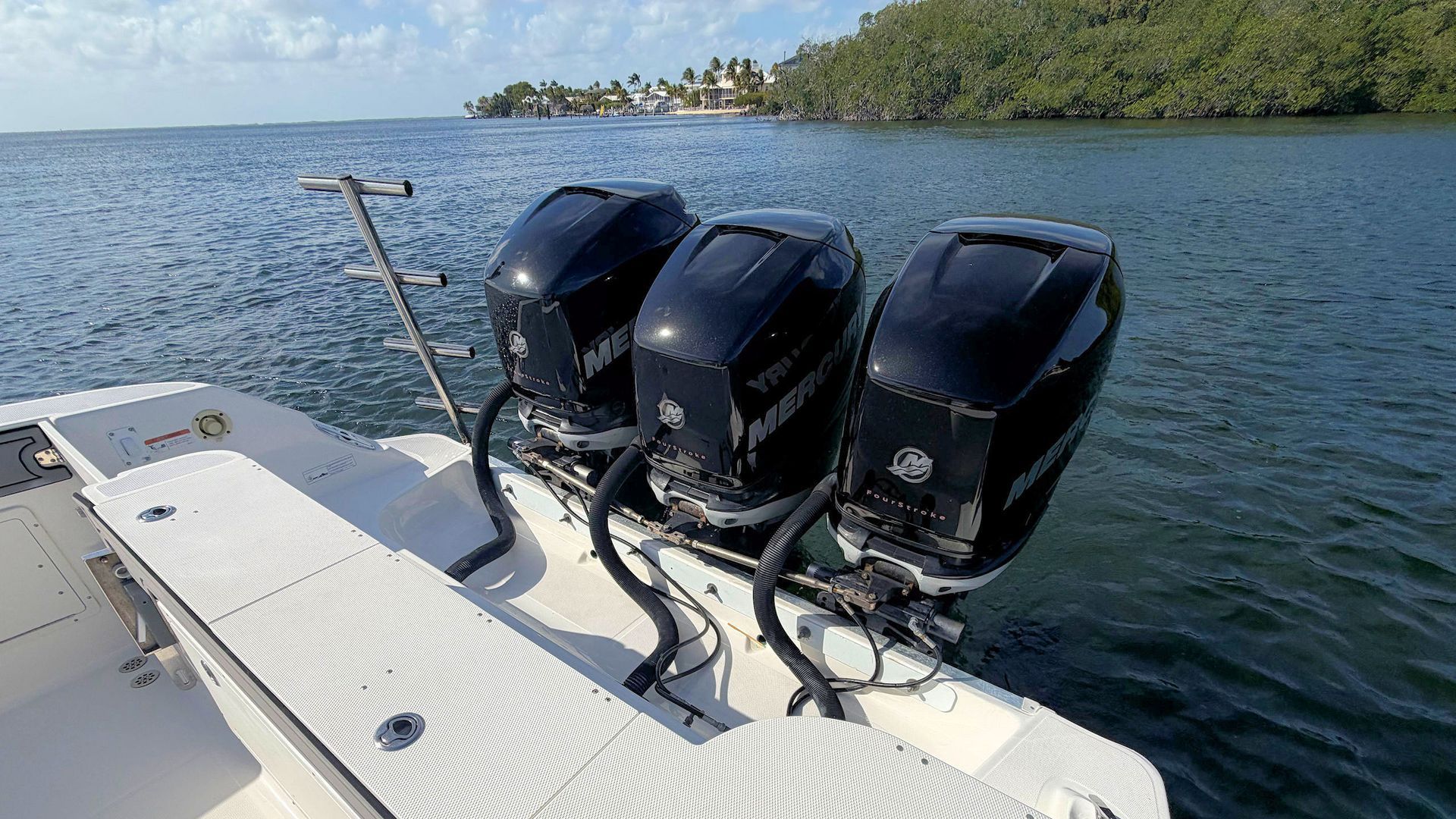 Three outboard motors on a boat’s stern above calm blue water near a green shoreline