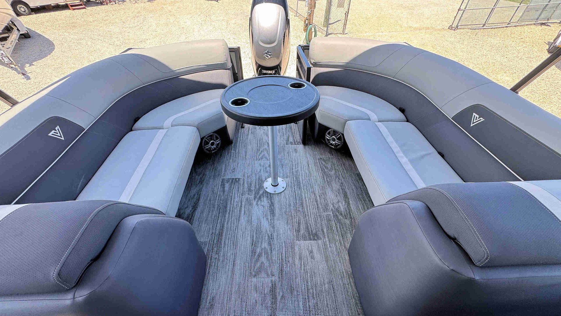 Boat deck with gray cushioned benches and a round table facing the outboard motor.