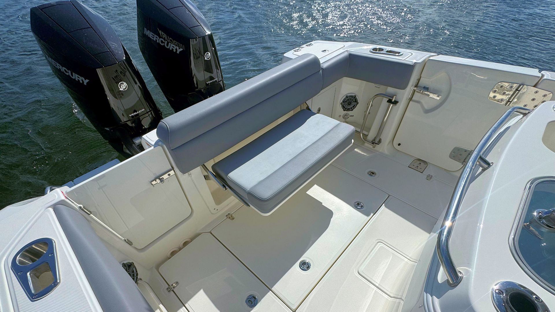 The stern of a Boston Whaler boat featuring gray cushioned seating, two black Mercury outboard motors, and white fiberglass deck.