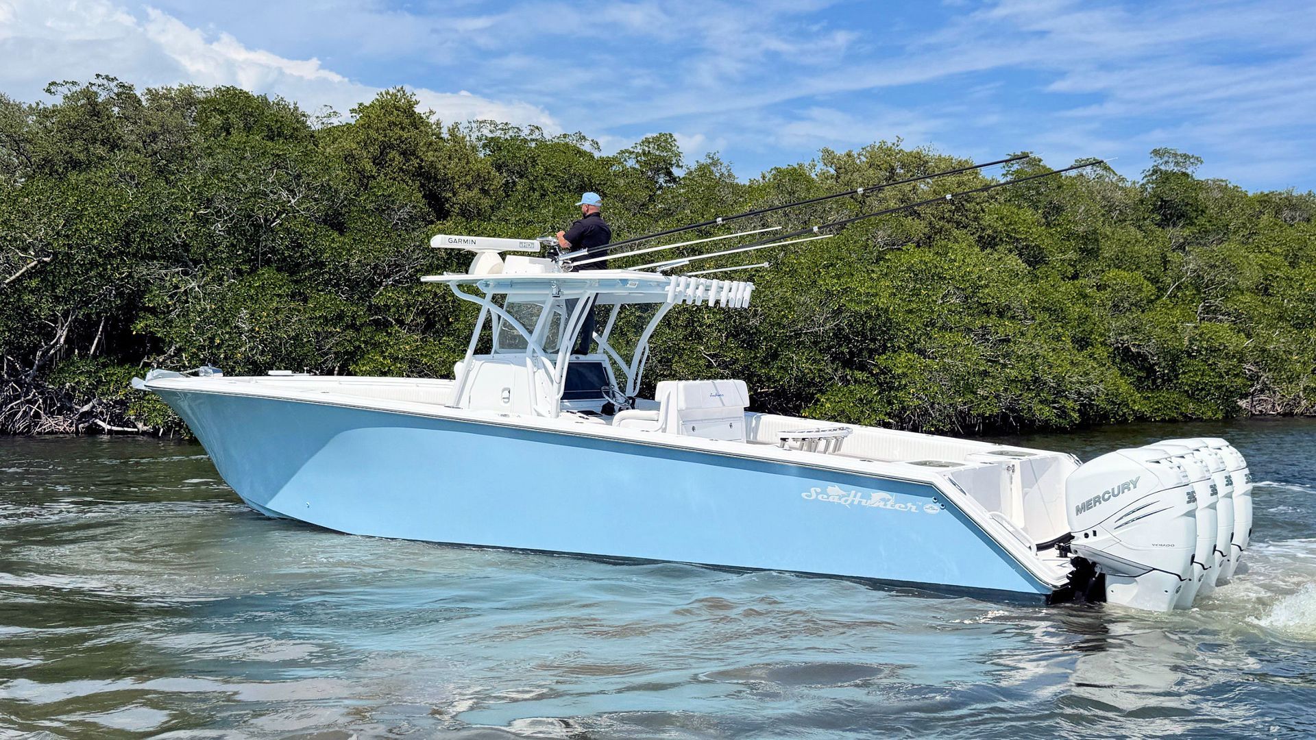 Light blue center console fishing boat cruising on choppy water near mangrove shoreline