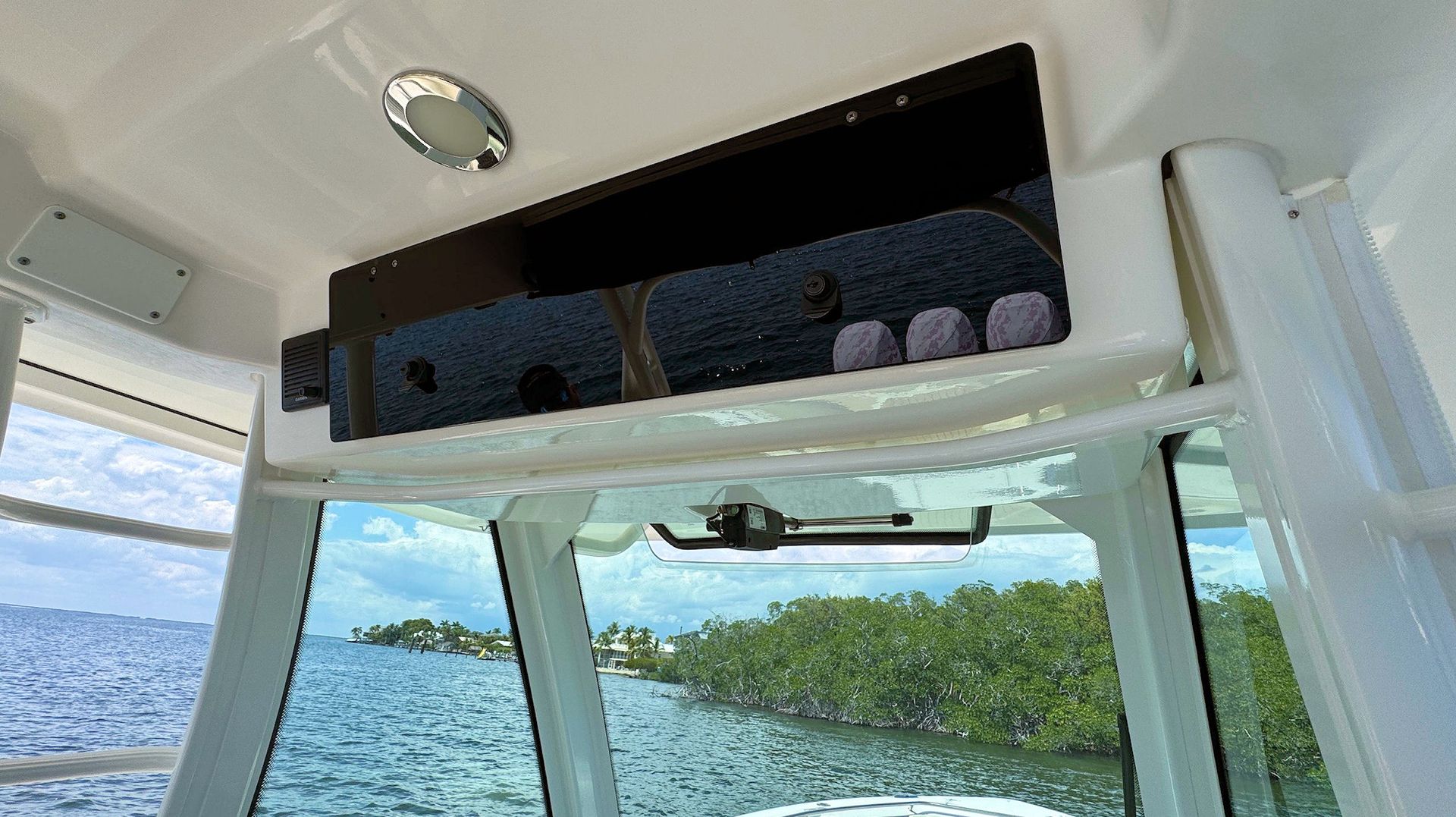Interior of a boat cabin with a black electronix compartment above large windows overlooking the sea.