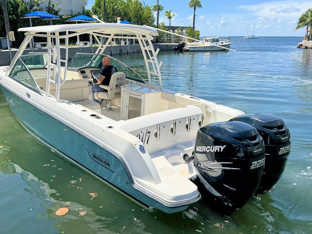 A blue and white motorboat with dual black outboard motors on the water with a person in the driver's seat.