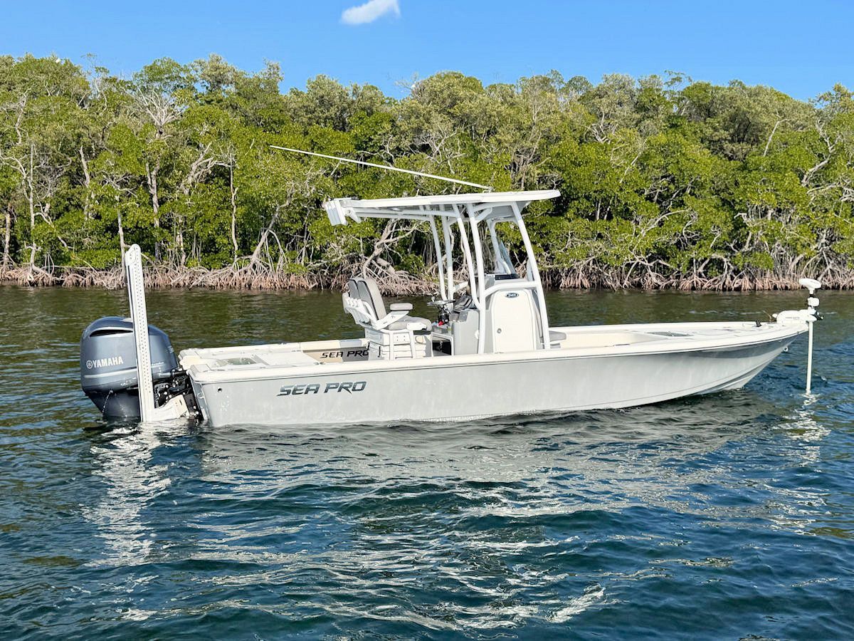 White fishing boat in water near mangroves under a blue sky.