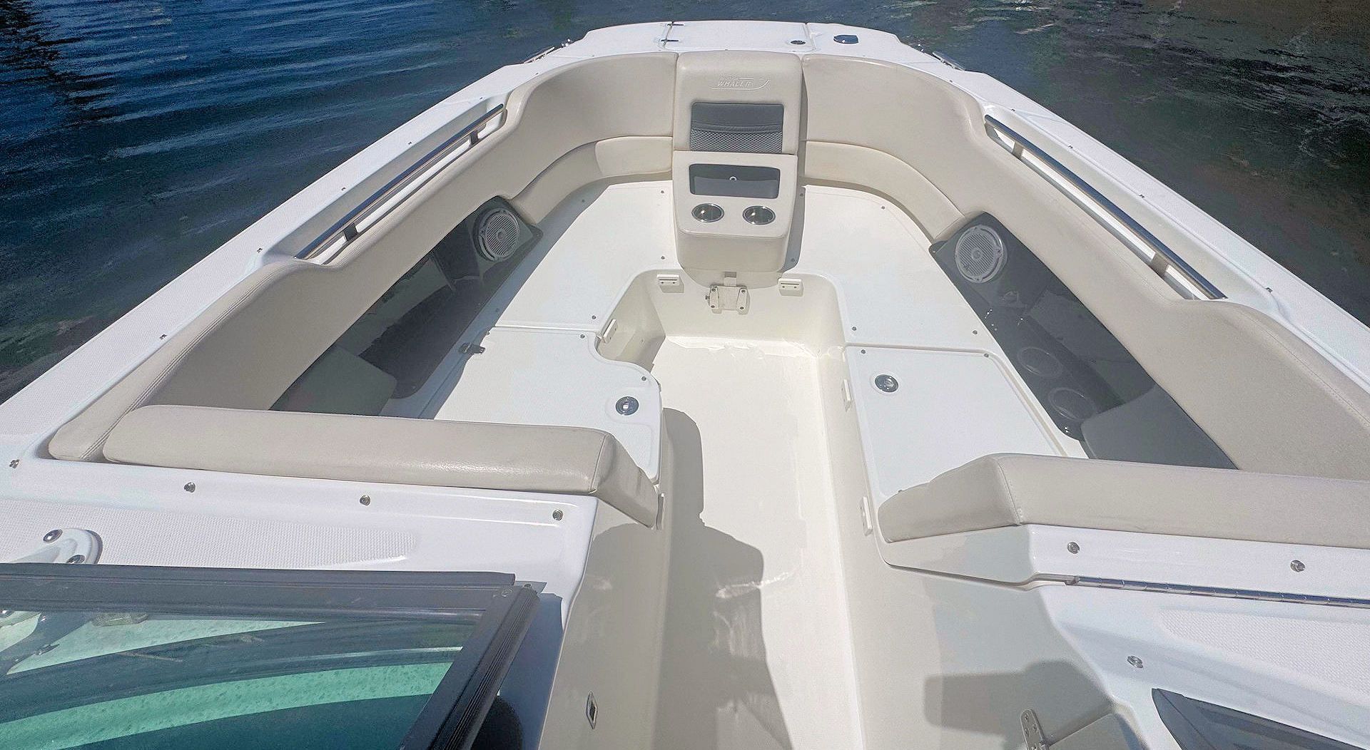 The bow seating area of a white boat with tan cushions, viewed from the windshield facing forward toward the water.
