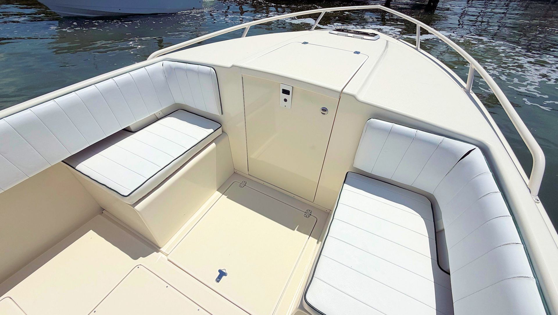 Boat bow seating area with cream cushions and white railings on calm water