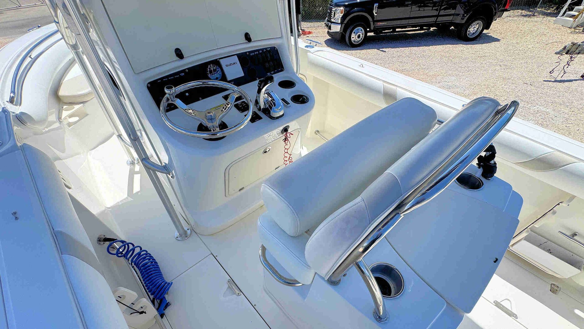 White boat helm with control panel, steering wheel, and cushioned helm seat on a sunny deck