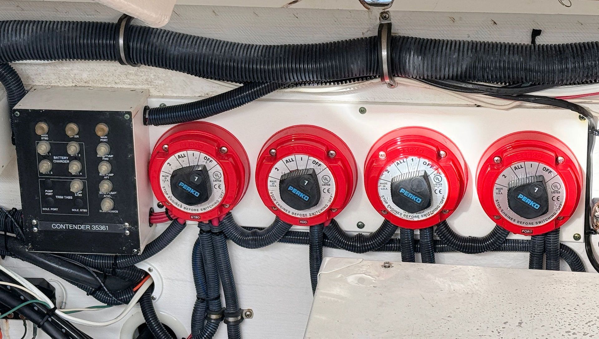 Electrical panel with four red rotary battery switches and a black control unit mounted on a wall.