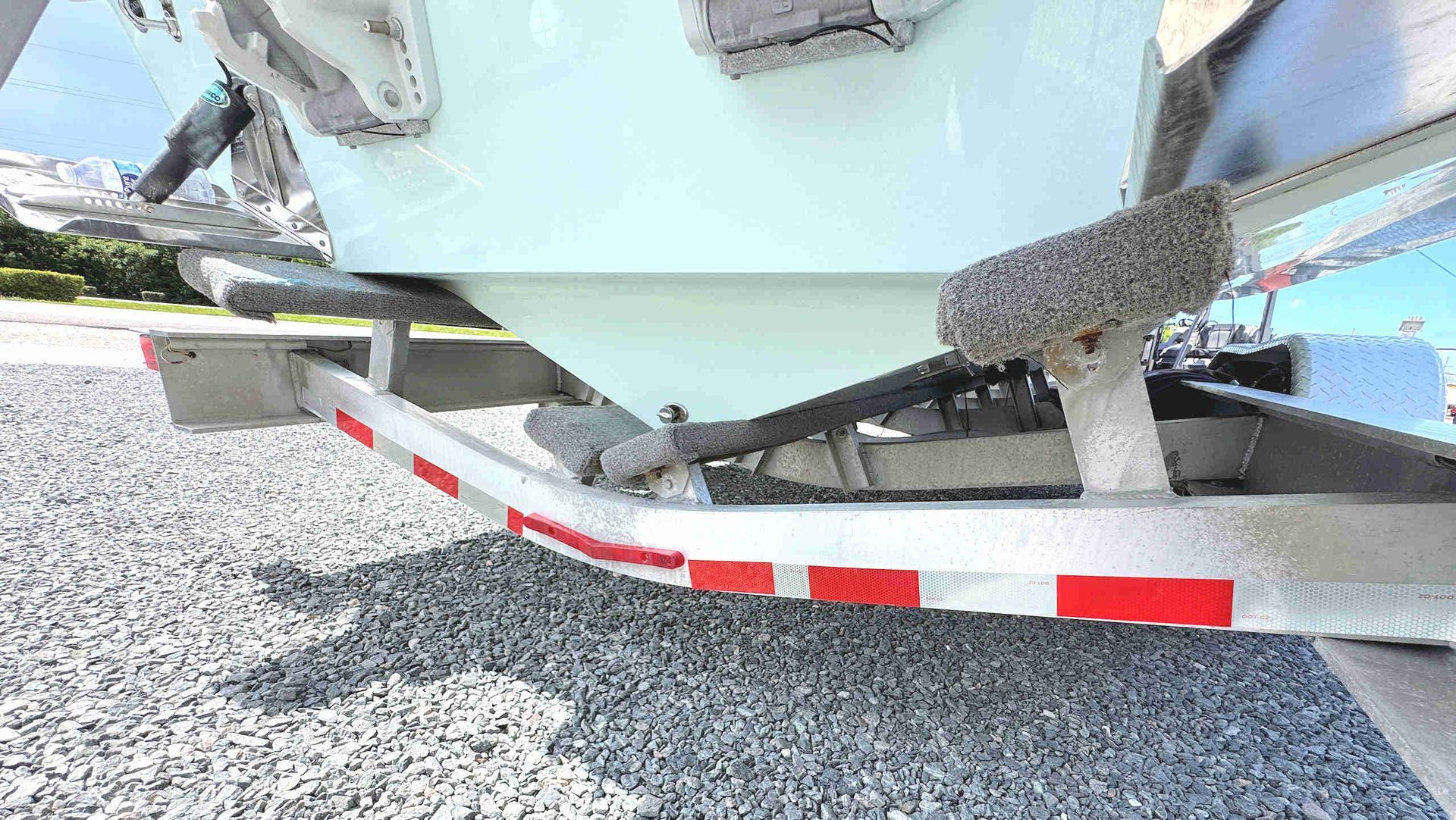 Boat hull on a trailer over gravel, with red-and-white reflective stripes visible underneath.