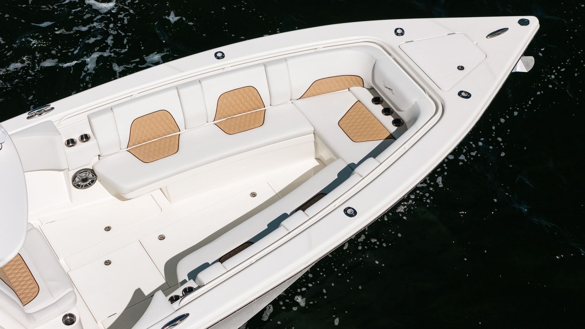 White motorboat bow with tan seats floating on dark water, viewed from above