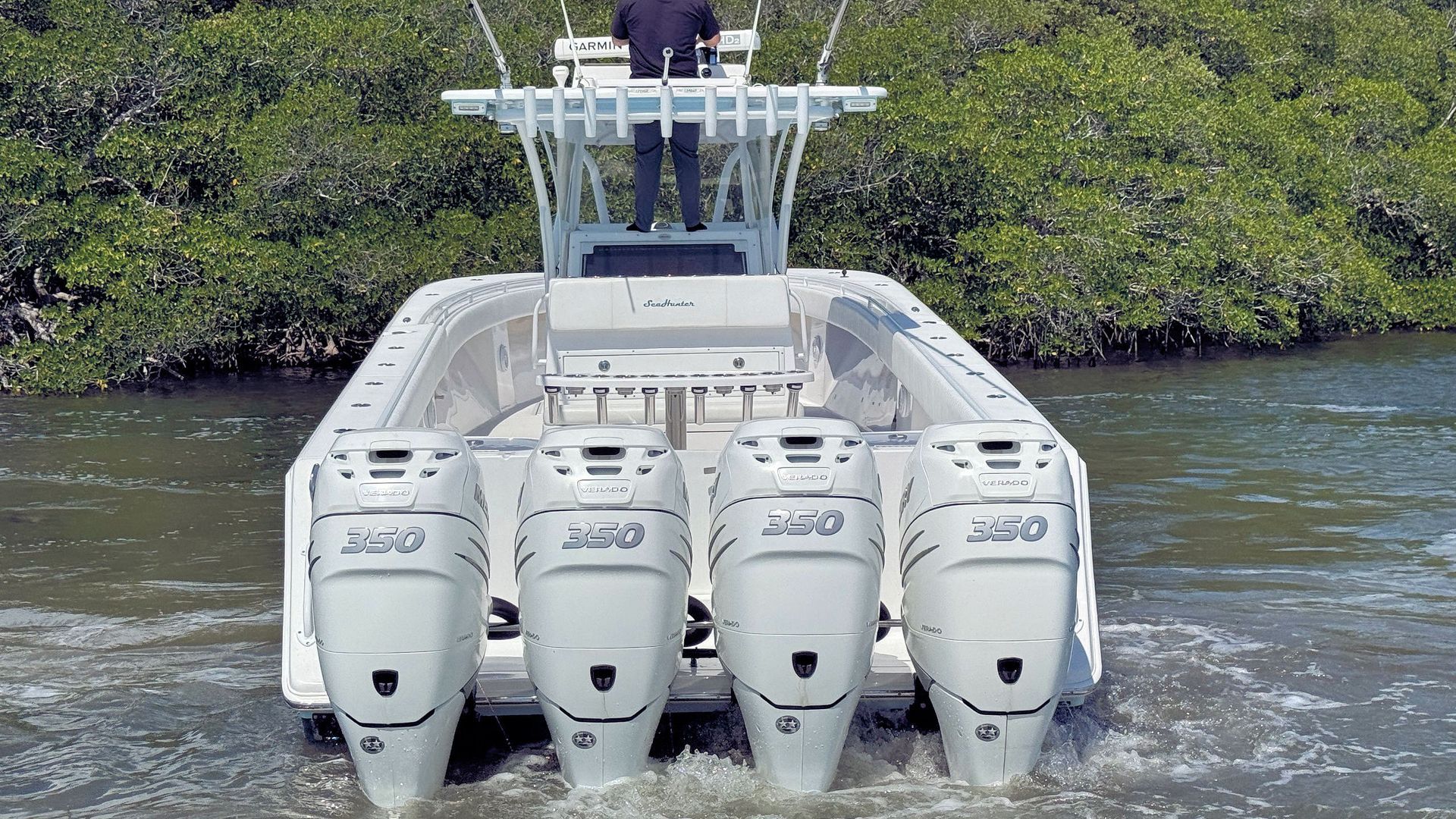 Light blue offshore fishing boat with multiple outboard motors heading through calm water near a green shoreline
