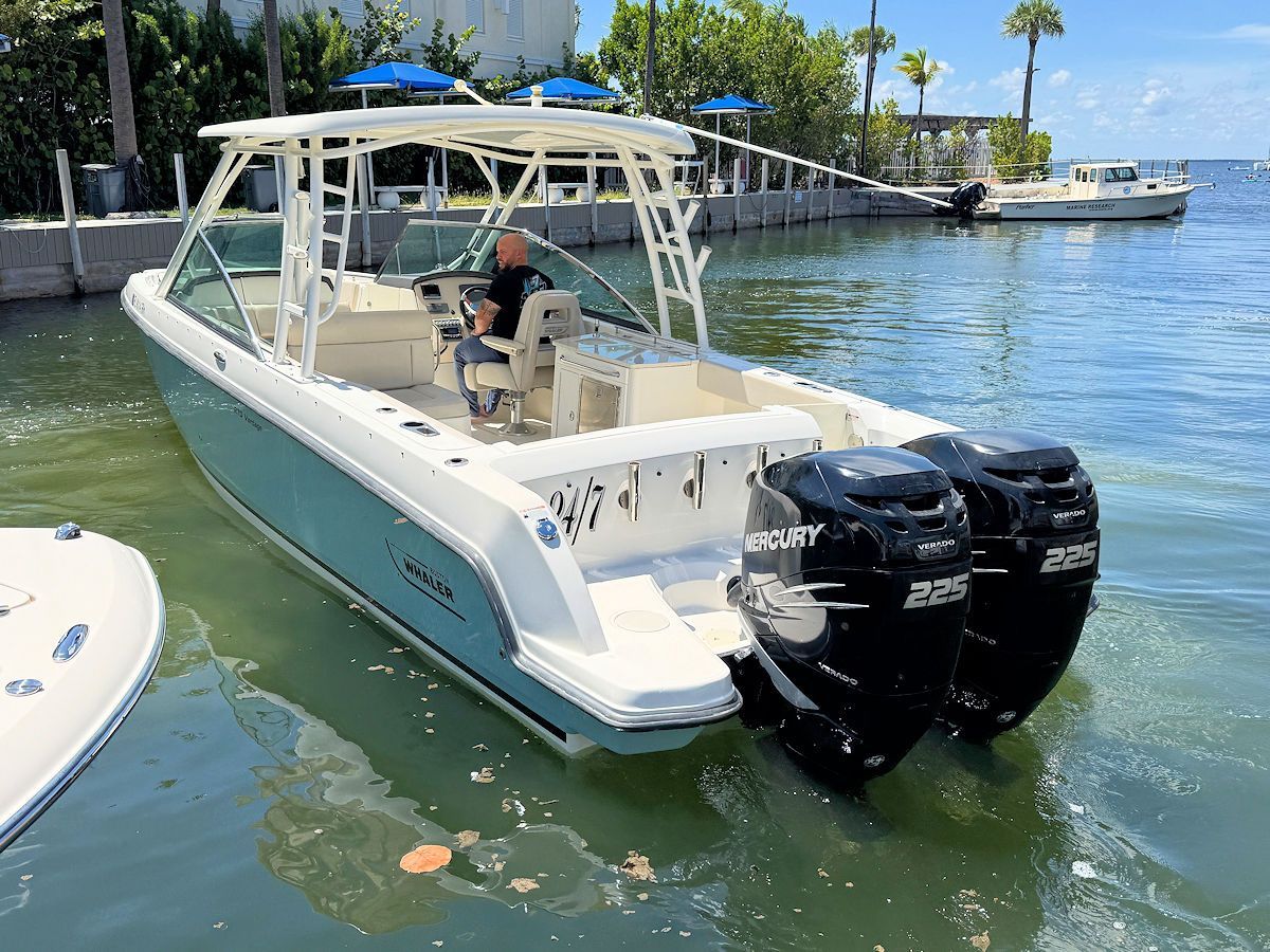 Boat with two black outboard motors in water, person at the helm.