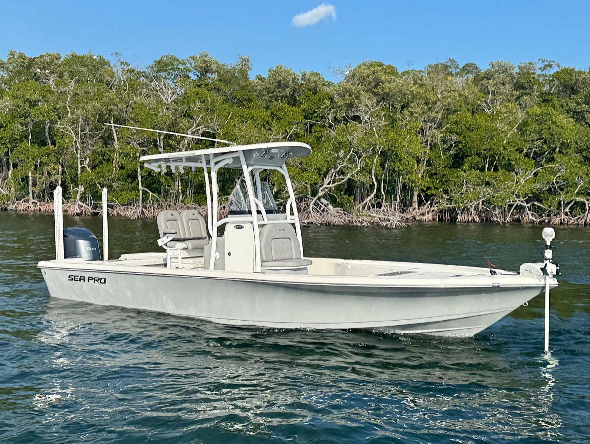 White fishing boat in water, with a mangrove backdrop.
