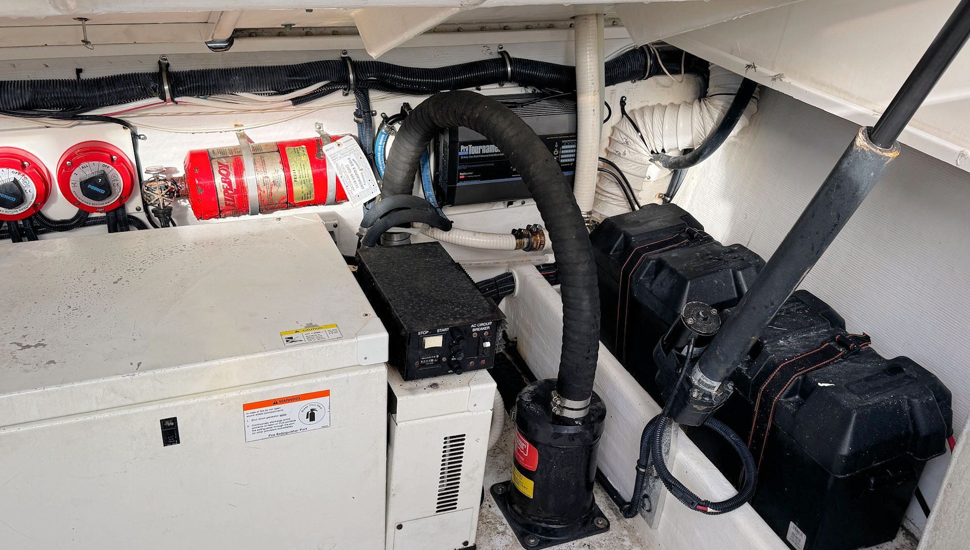 Boat engine compartment with white machinery, black hoses, and red fire extinguishers