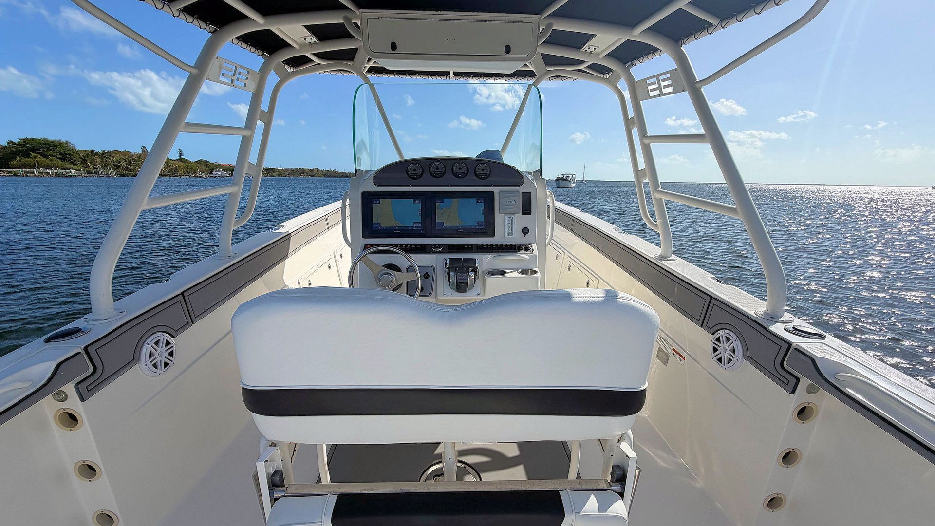 View from a boat’s cockpit over blue water, with white helm seats and a canopy overhead.