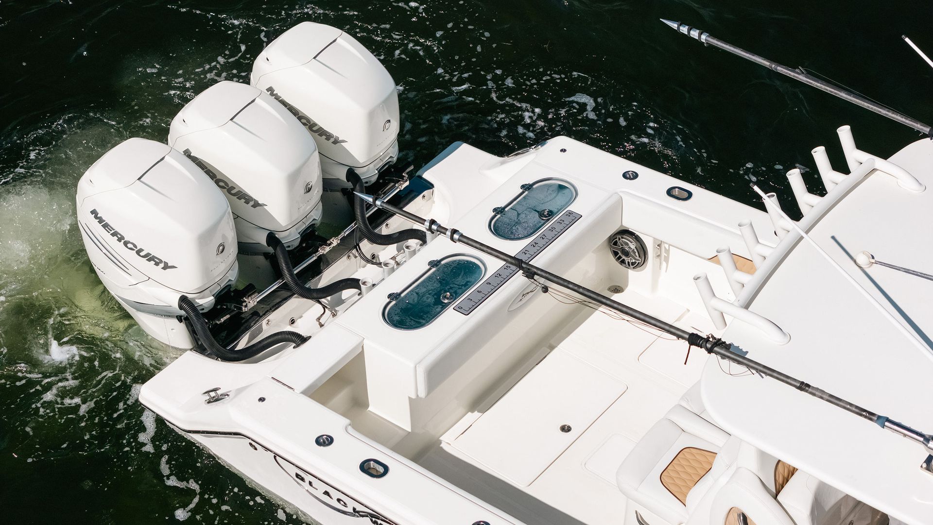 White yacht stern with three outboard motors on dark green water, aerial view