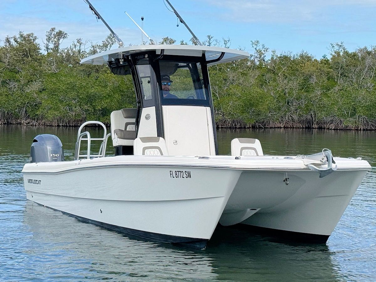 White catamaran boat on the water with a cabin, fishing rods, and mangroves in the background.