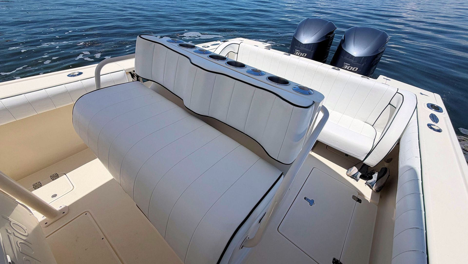 White cushioned bench on a boat deck with ocean water and twin outboard motors in the background