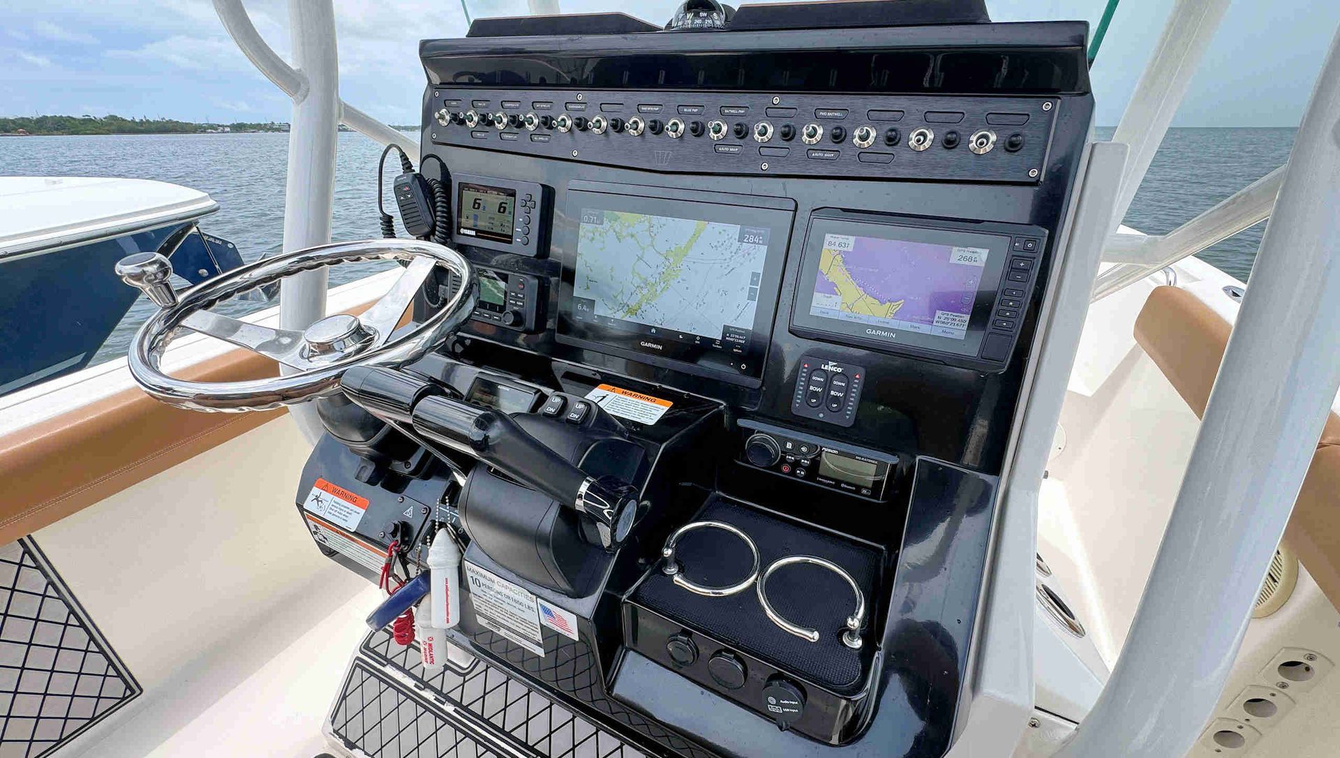 Boat helm station with navigation screens, switches, and steering wheel on a sunny deck