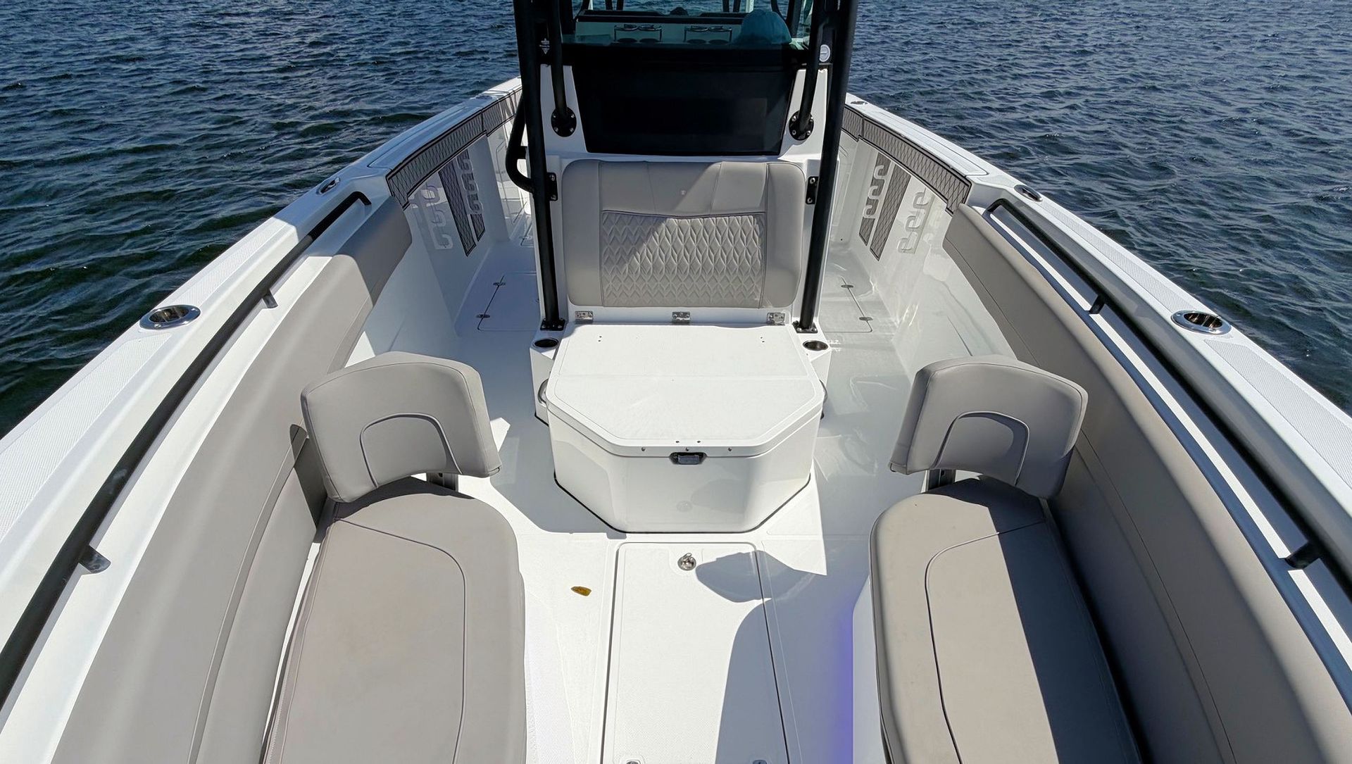Empty white boat deck with gray seats and a console on open water