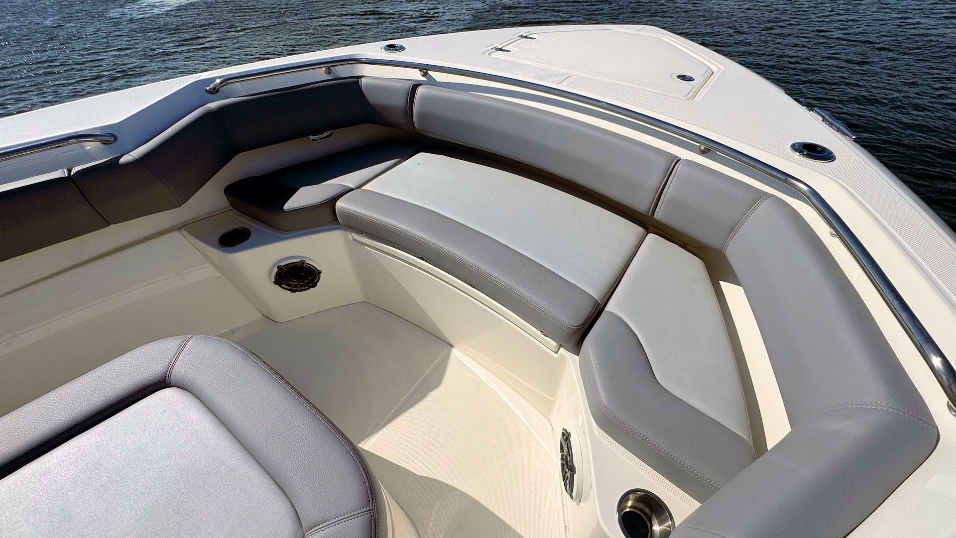 The bow area of a boat features cream-colored seating with grey cushions, a metallic cup holder, and a view of open water.