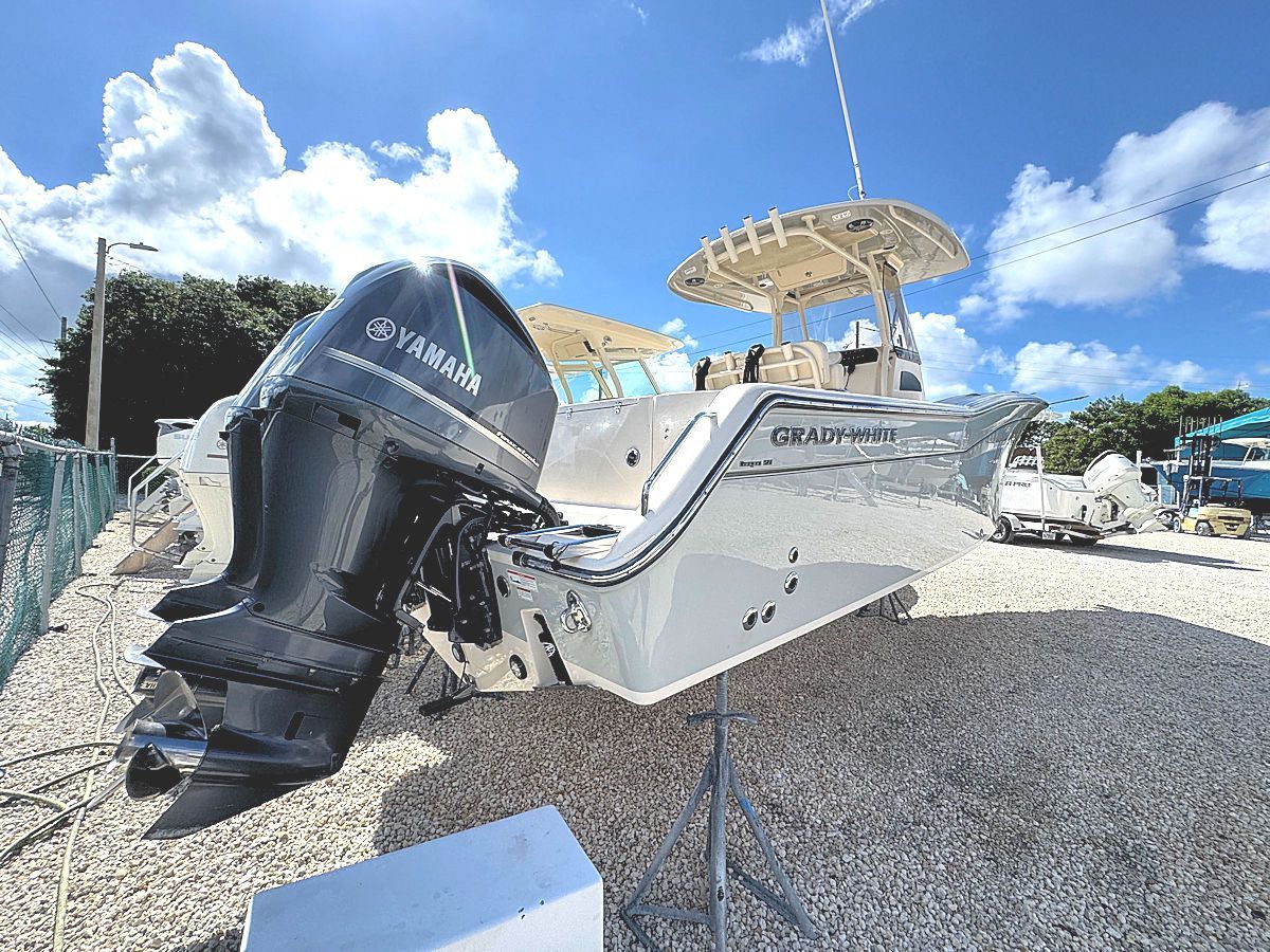 A white boat with black Yamaha engines on a gravel surface under a blue sky.