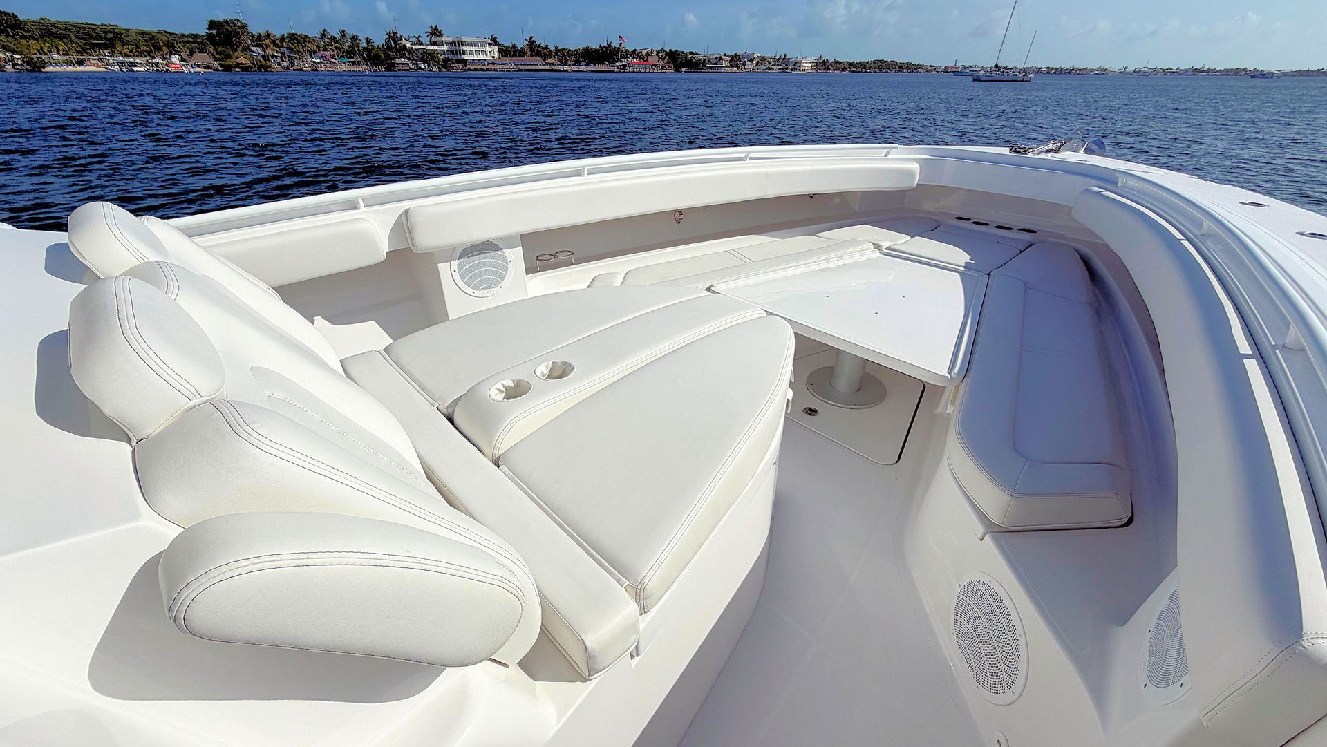 White boat deck seating on calm blue water with shoreline in the distance