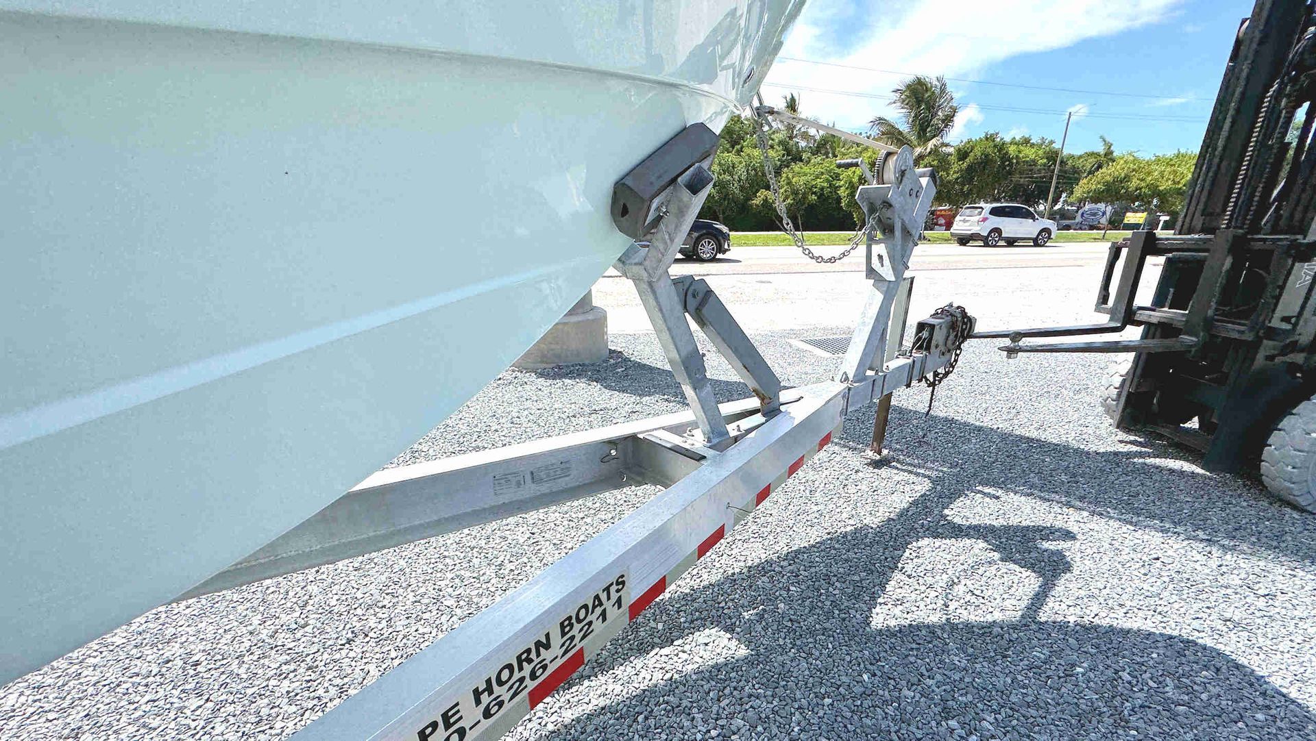 Boat trailer supporting a white boat on gravel in a sunny parking lot