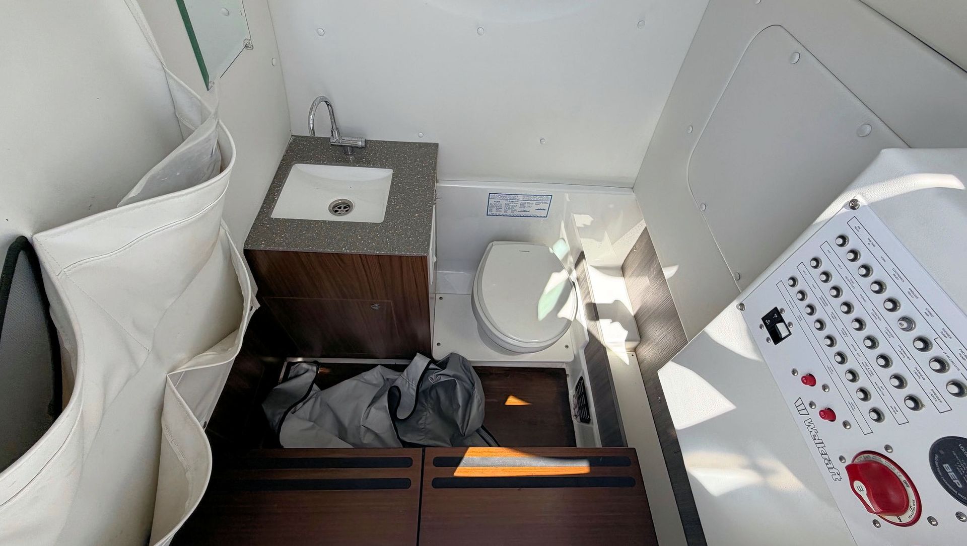 Center console cabin with head and wood drawers, white cushions, a hose, and a control panel on the right.