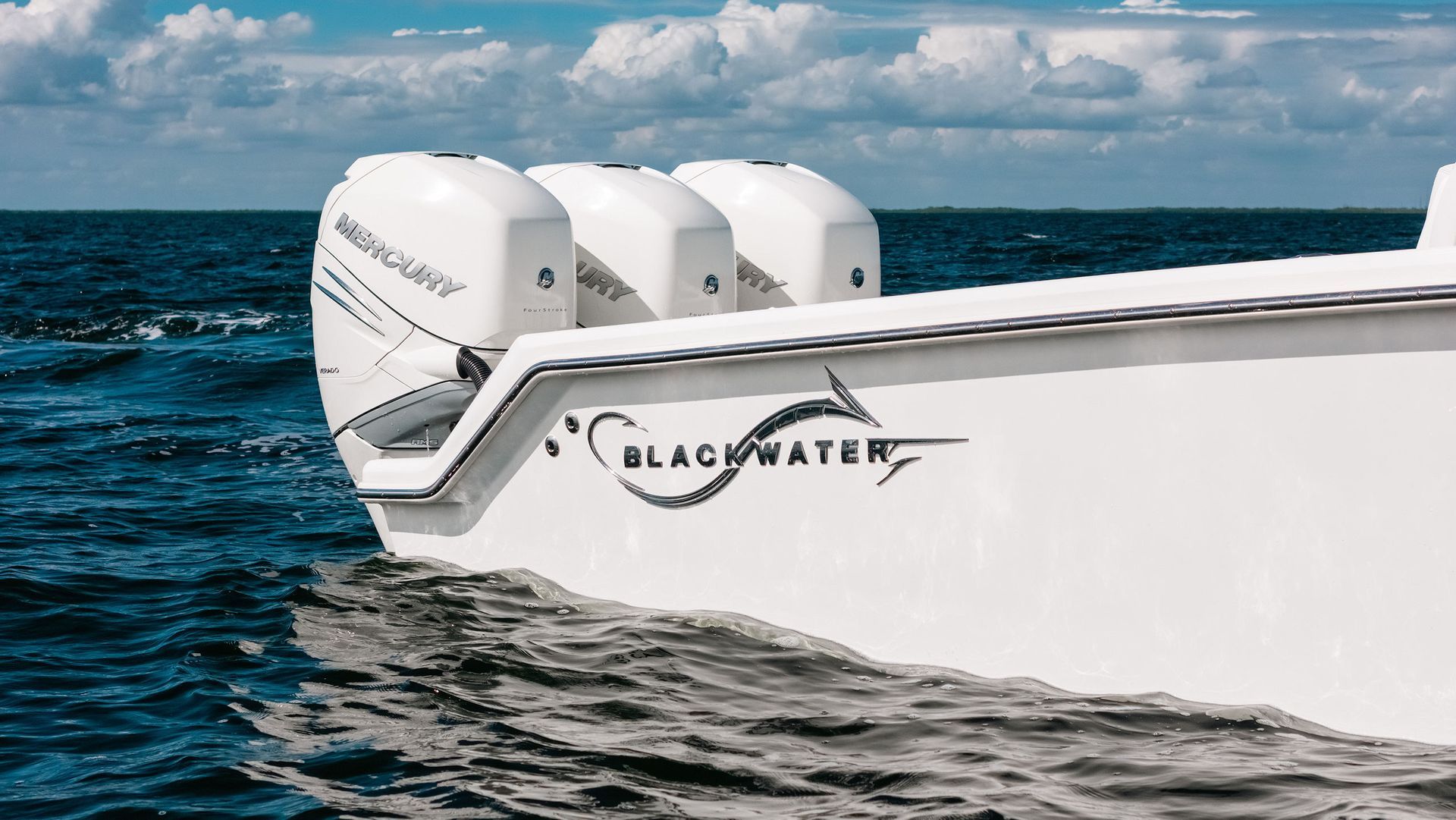 White boat stern with three outboard motors on choppy blue ocean under cloudy sky