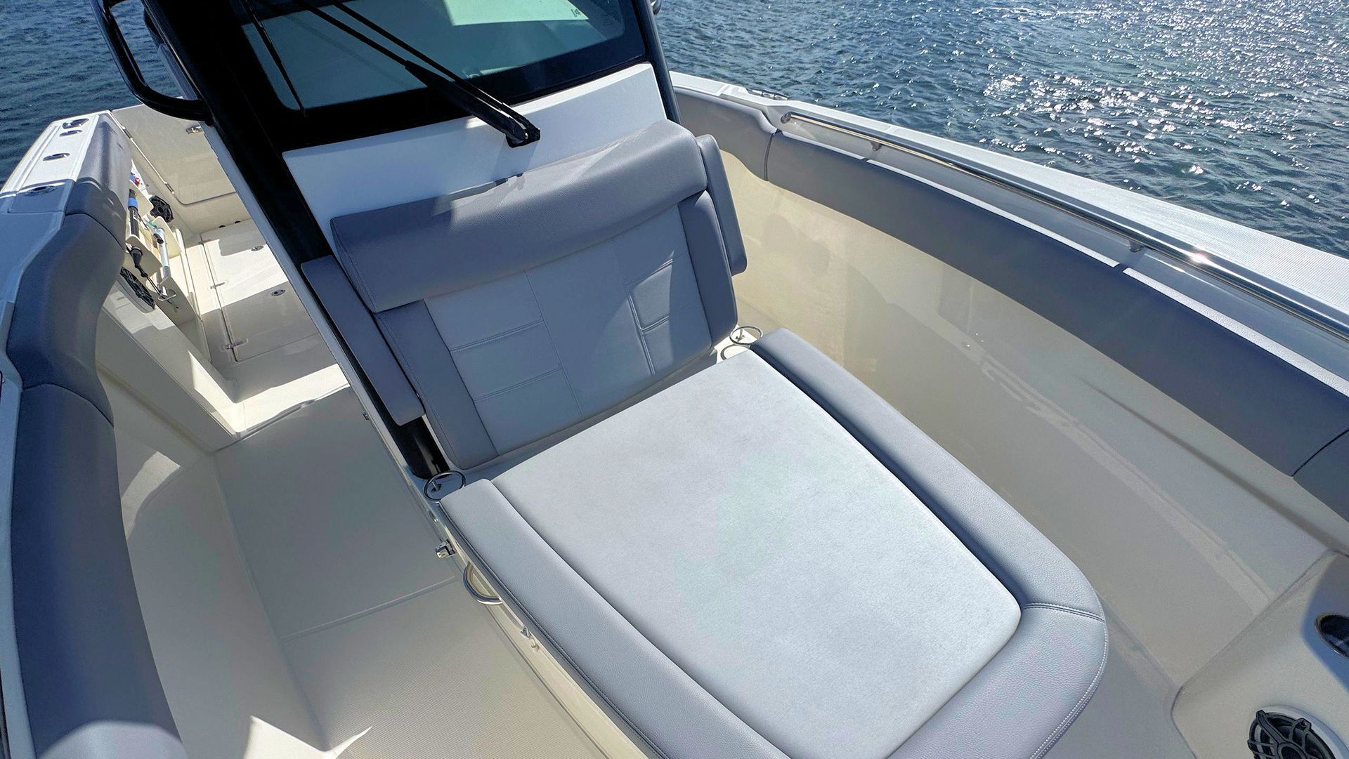 The interior of a boat showing a gray upholstered bench seat located in the bow area, with water visible in the background.