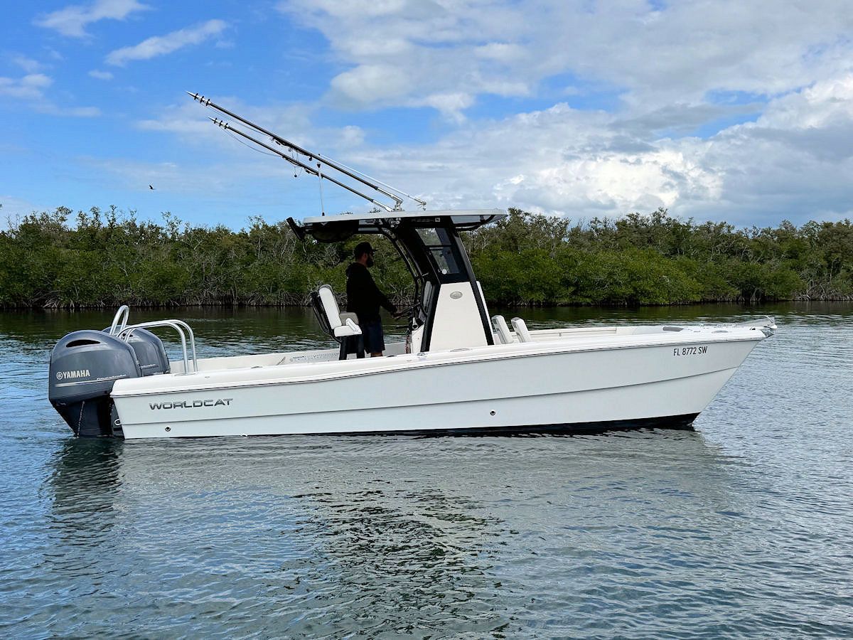 White motorboat on water with person at helm, fishing rods, and mangrove trees in background.