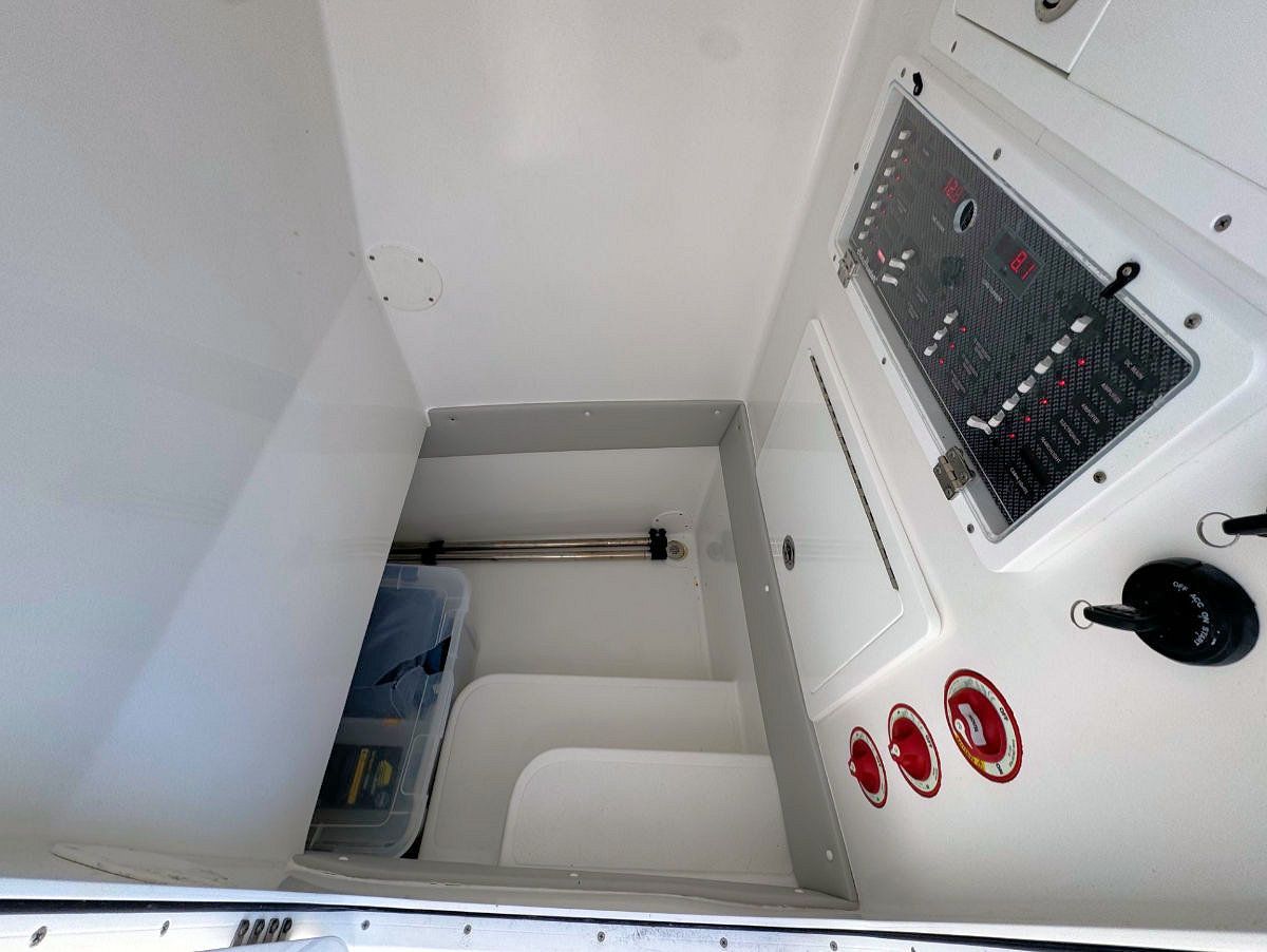 Interior of a boat with steps leading down to a storage area. White walls, control panel, red accents.