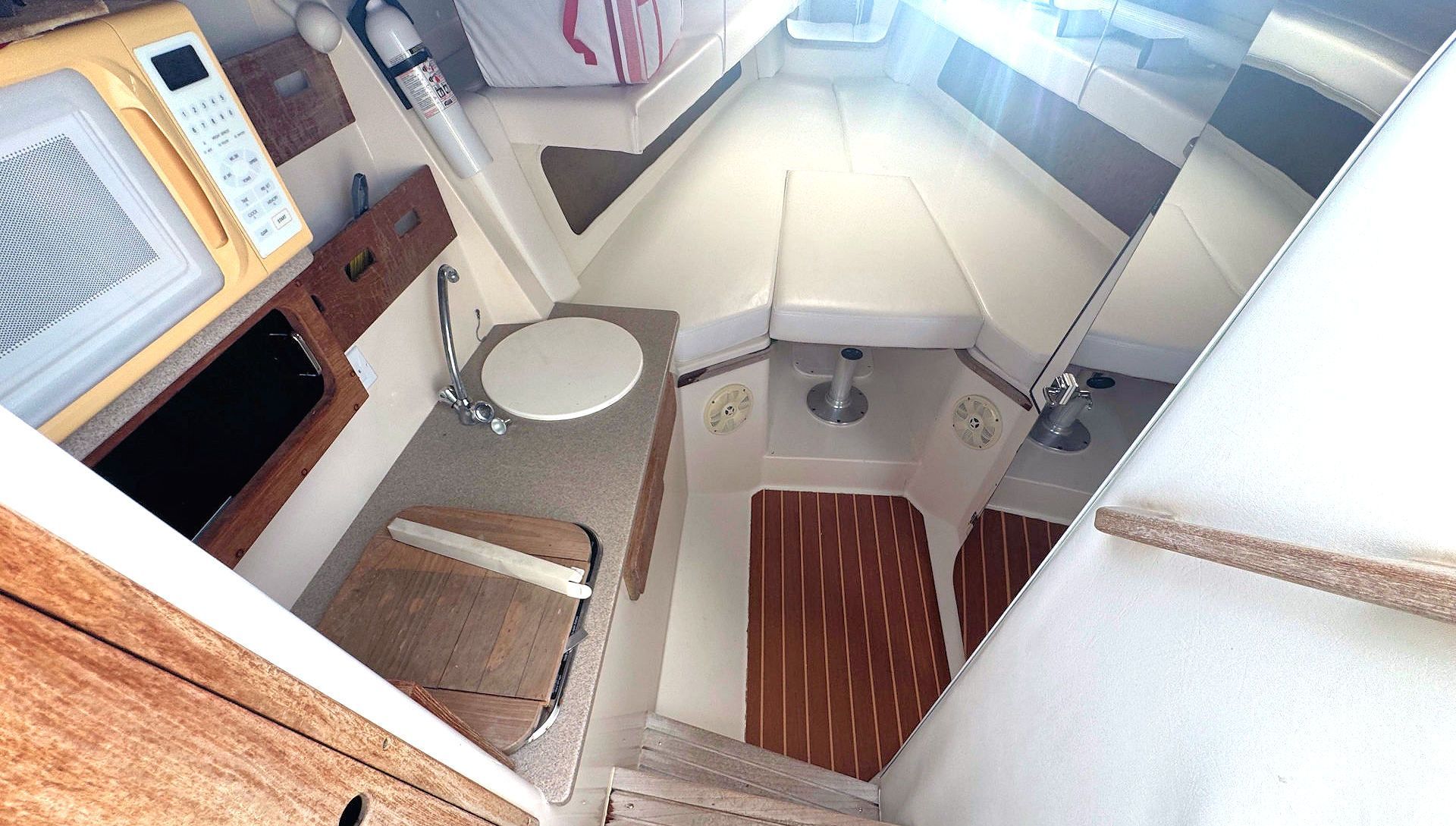 Compact boat cabin with a sink, toilet, wood accents, and a skylight above.