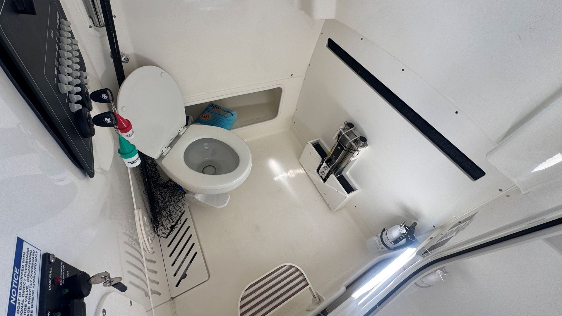 A high-angle view of a white, compact boat head featuring a toilet, a small sink, and a striped folding seat.