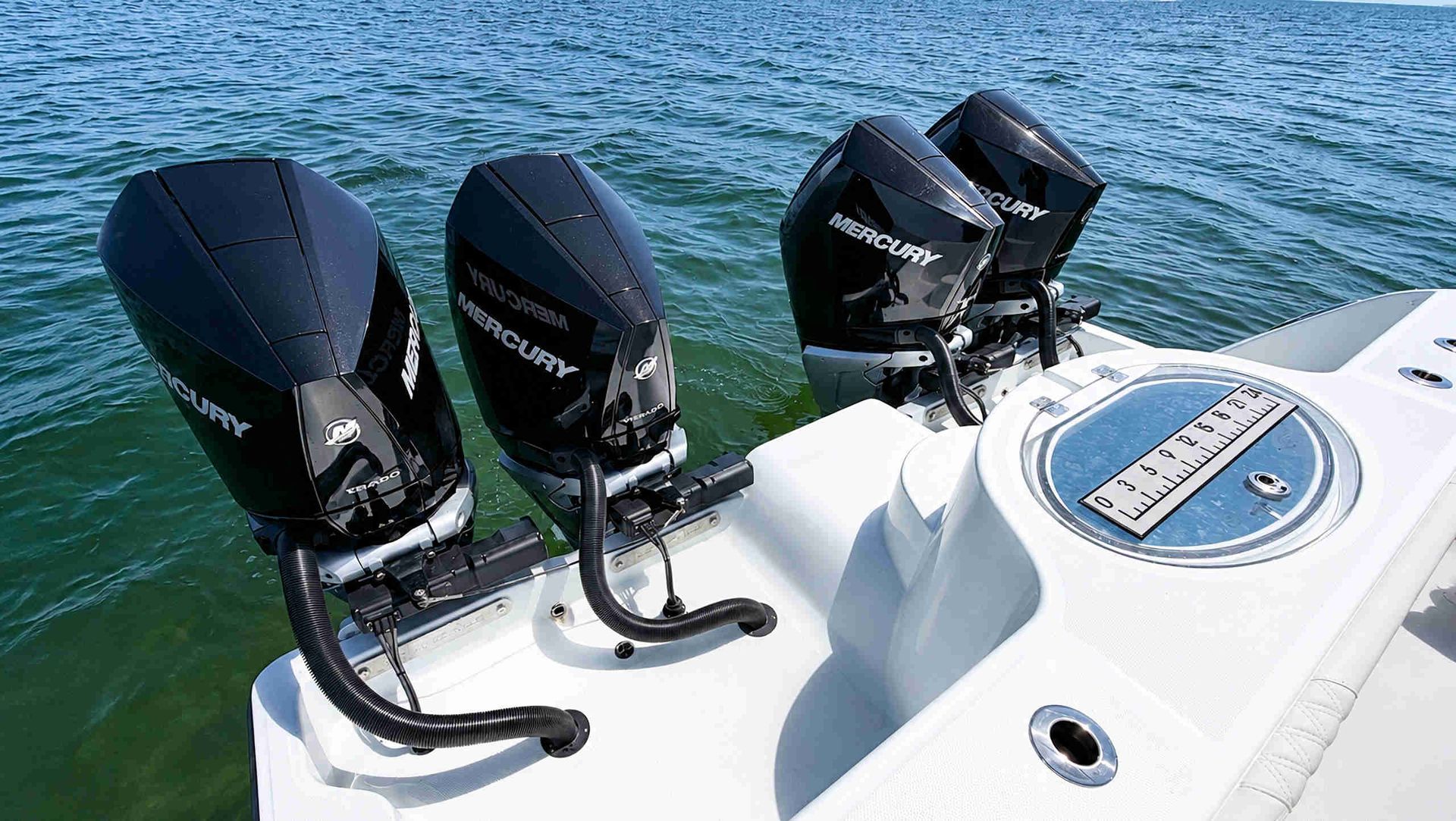 Four black outboard motors on a white boat with blue water in the background