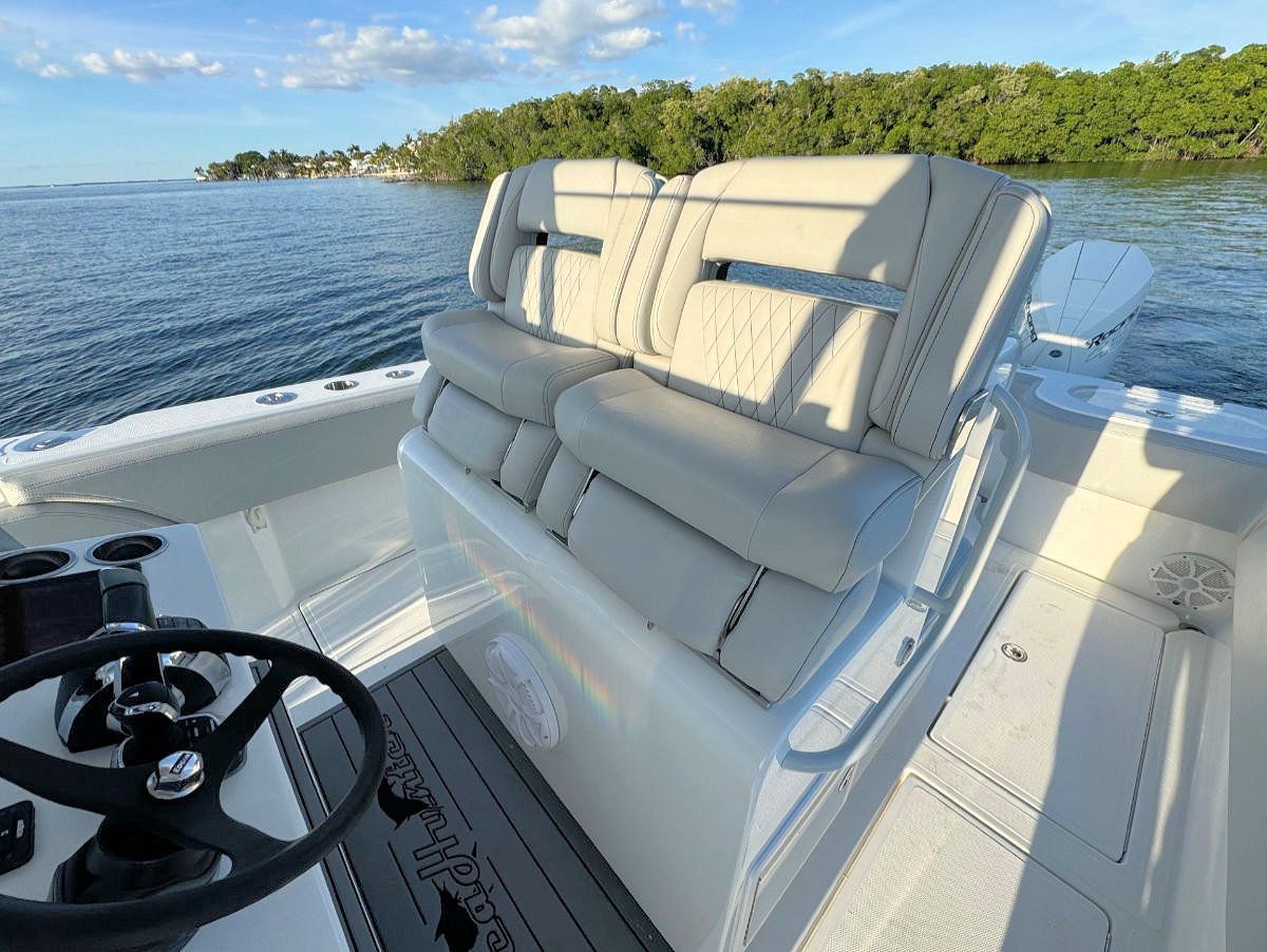 Interior of a white boat with cream-colored seats and a steering wheel, on calm water.