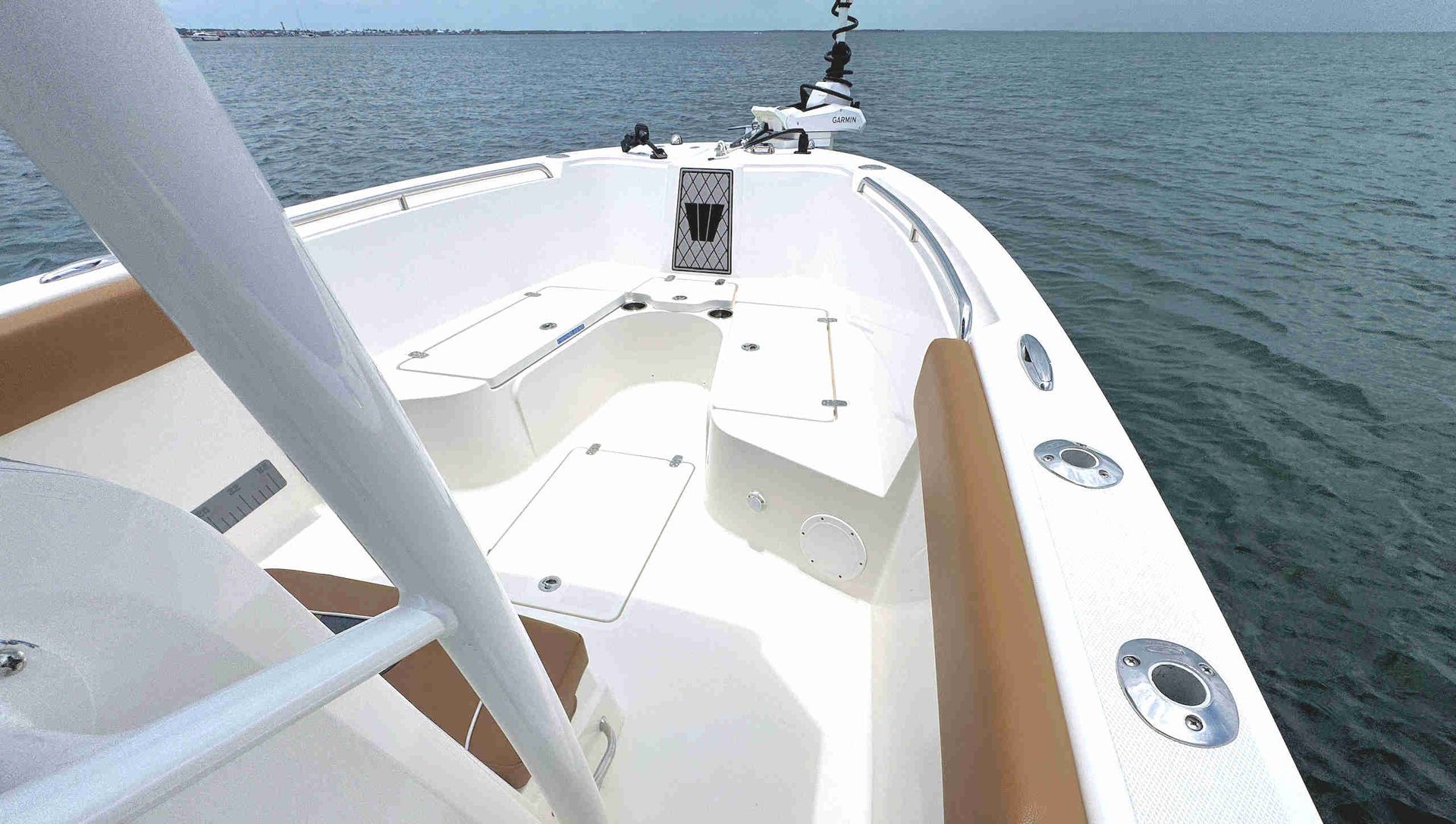 White boat deck with railings and a small seat, cruising on calm blue water.