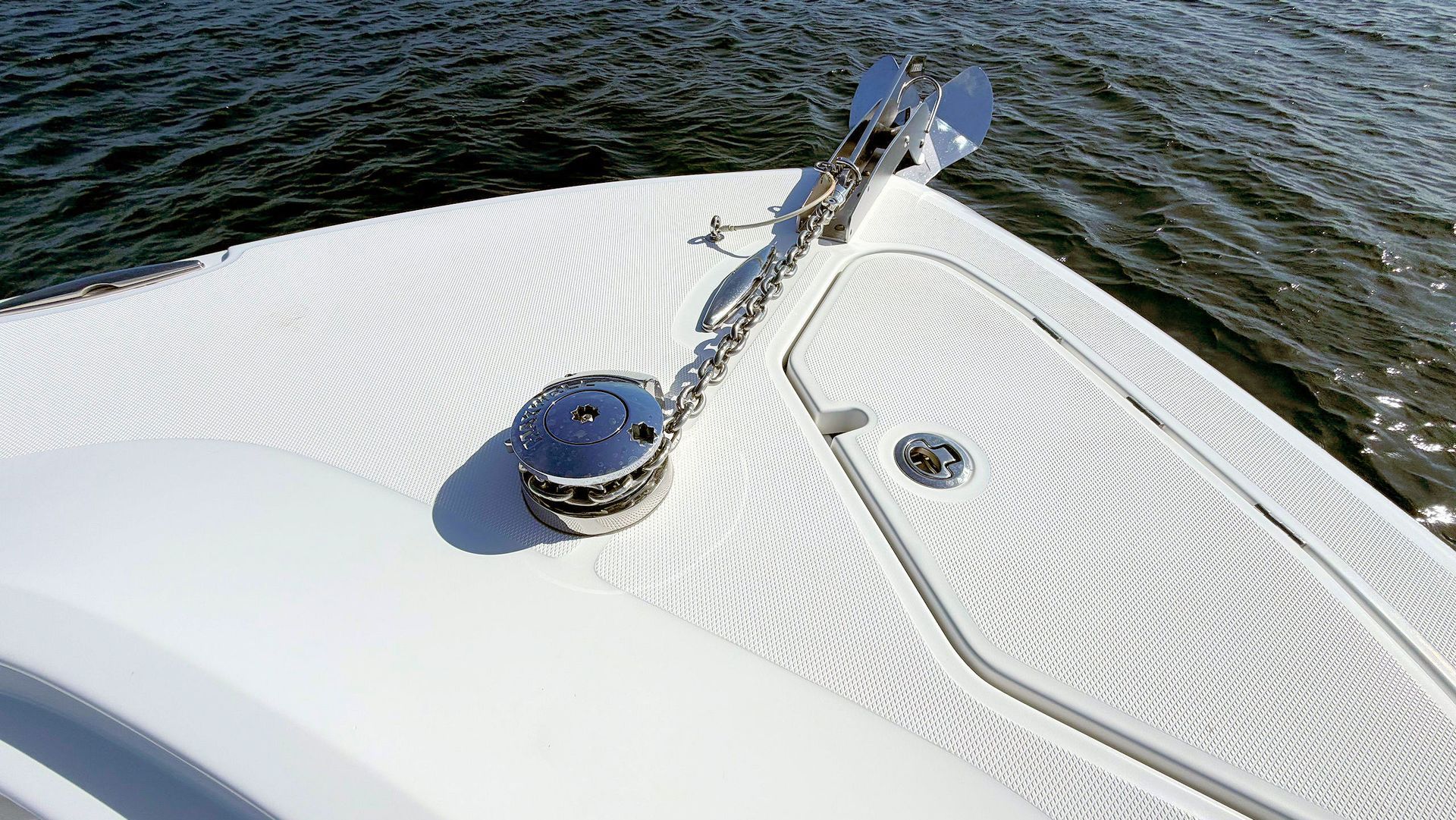 White boat deck with anchor windlass and mooring cleat beside rippling water