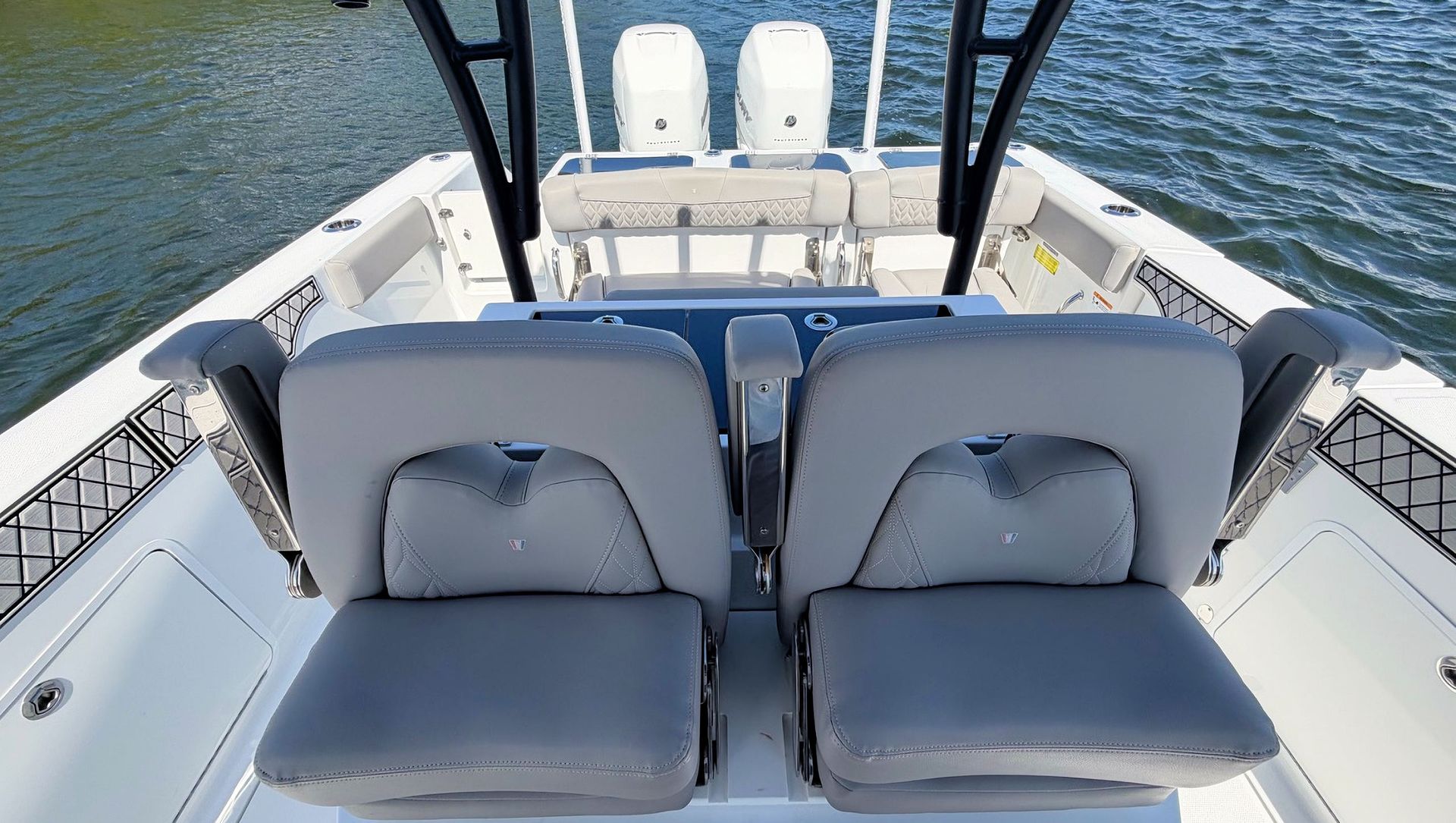 Two gray cushioned seats on a boat deck facing the water and stern bench seats