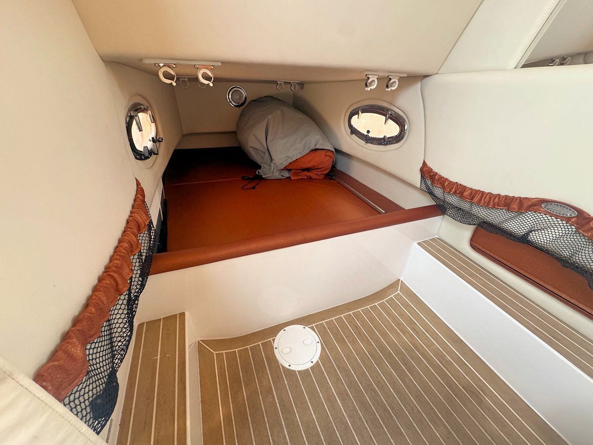 Interior of a boat cabin with a sleeping area. Brown, white, and wood tones are prominent.