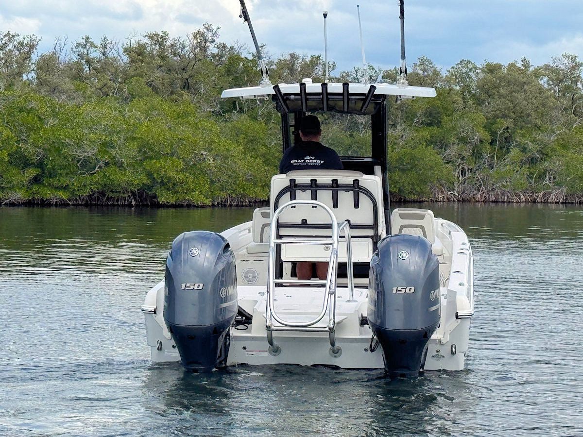 Motorboat on water with two outboard motors, driver, and mangroves in the background.