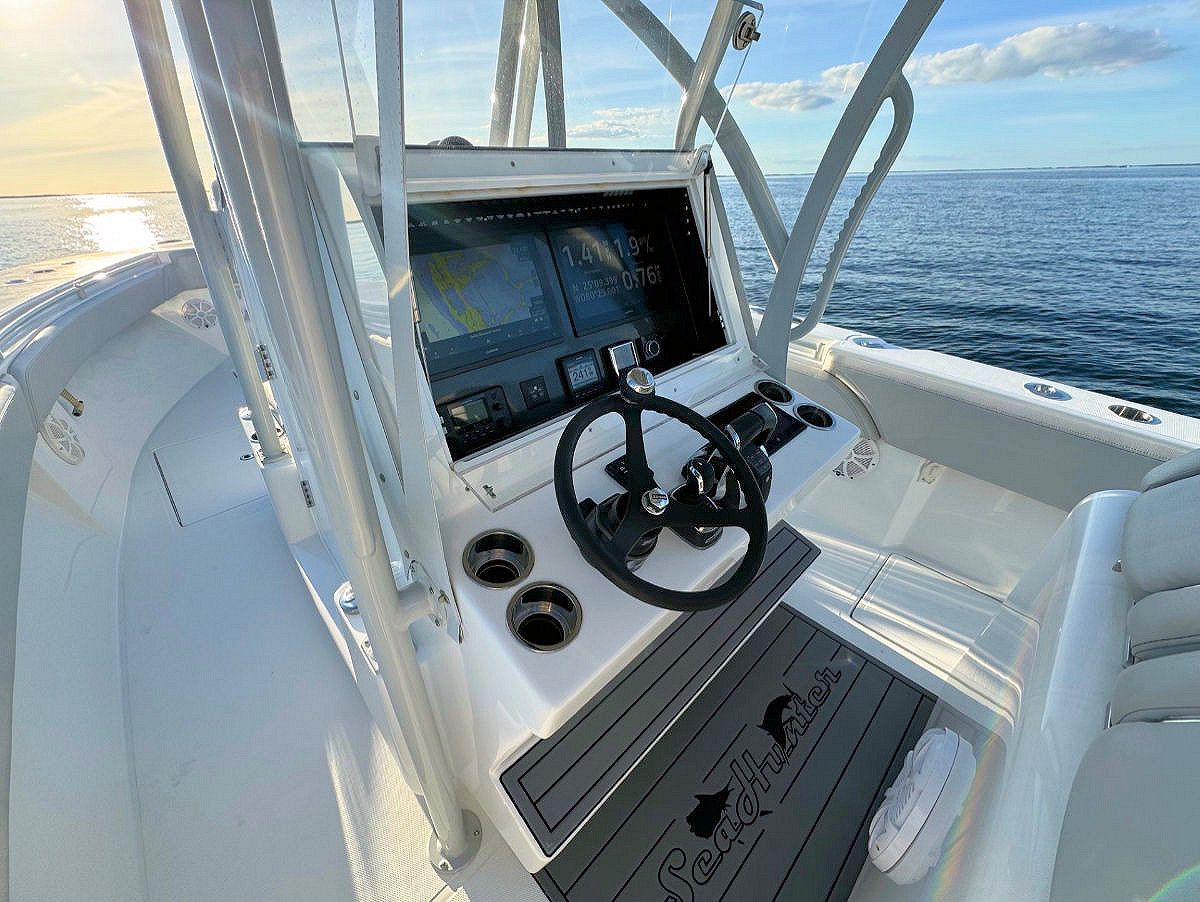 Interior of a white boat's helm, featuring a steering wheel, navigation screens, and cup holders. The sea and sky are in the background.