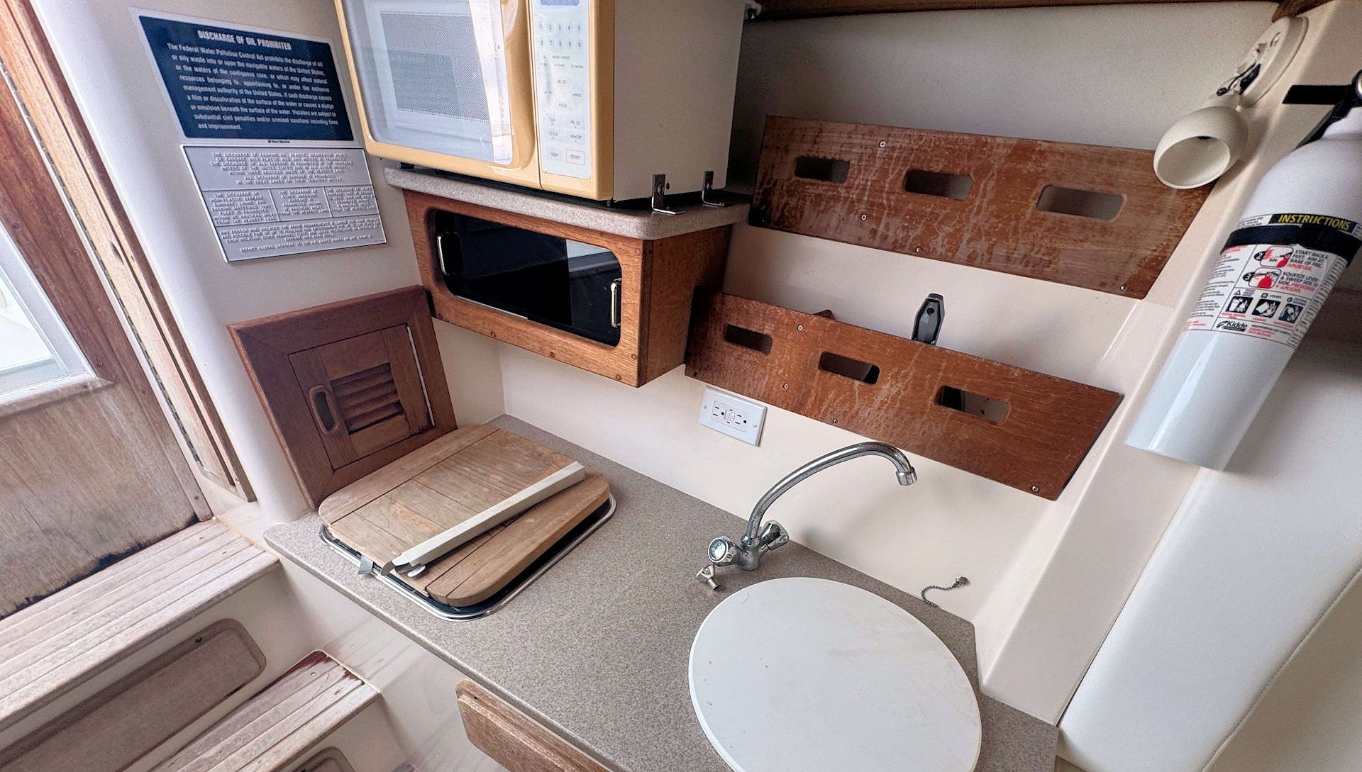 Compact bathroom with sink, mirrored cabinet, wooden shelves, and a fire extinguisher on the wall