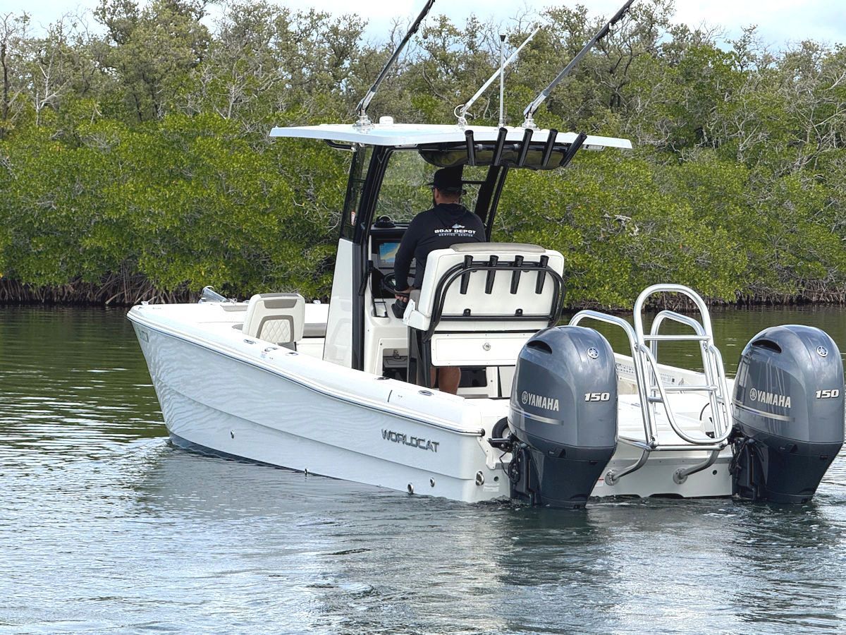 White motorboat on water, person at helm, two outboard motors, mangroves in background.
