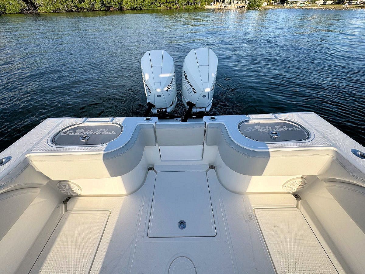 Boat stern with two outboard motors, white interior, overlooking water.